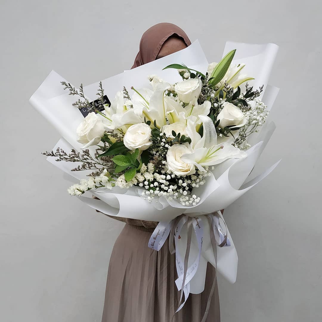 A large bouquet of white flowers with green leaves, wrapped in white paper and tied with a ribbon. flower bouquet surabaya, buket bunga surabaya, jakarta, florist jakarta, bouquet jakarta.