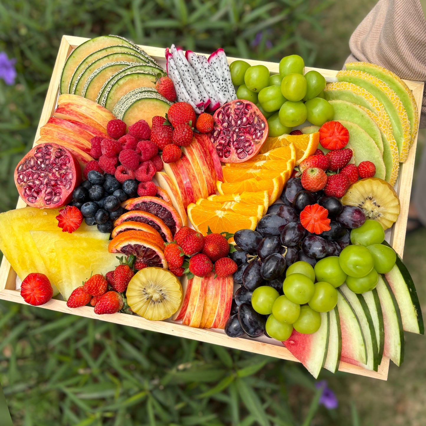 Assorted fruits on a wooden tray with a blurred green outdoor background. Colorful Fruit Platter Jakarta & Surabaya – Le Bliss Platter. best Fruit platter surabaya, best fruit platter jakarta