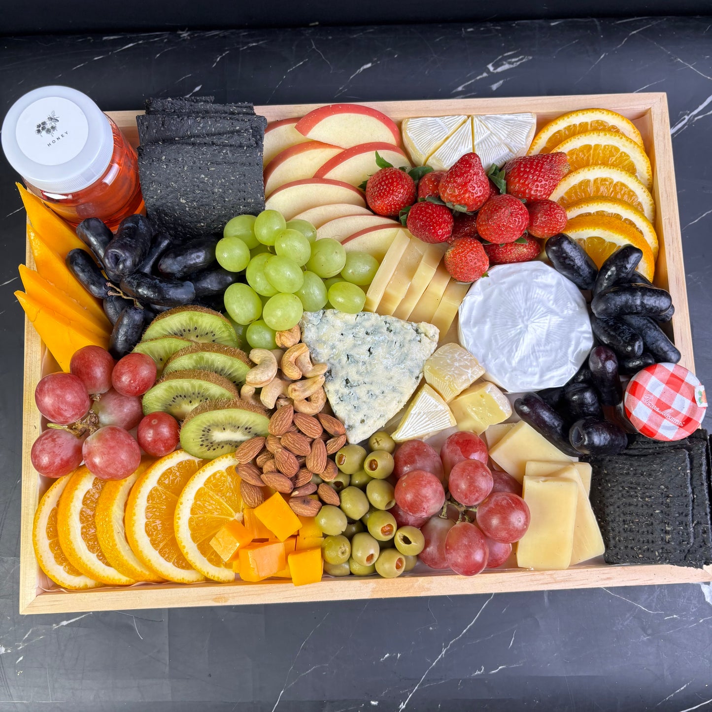 Blue cheese platter with wheat crackers, fresh fruit, and nuts on a wooden charcuterie board, ready for delivery in jabodetabek