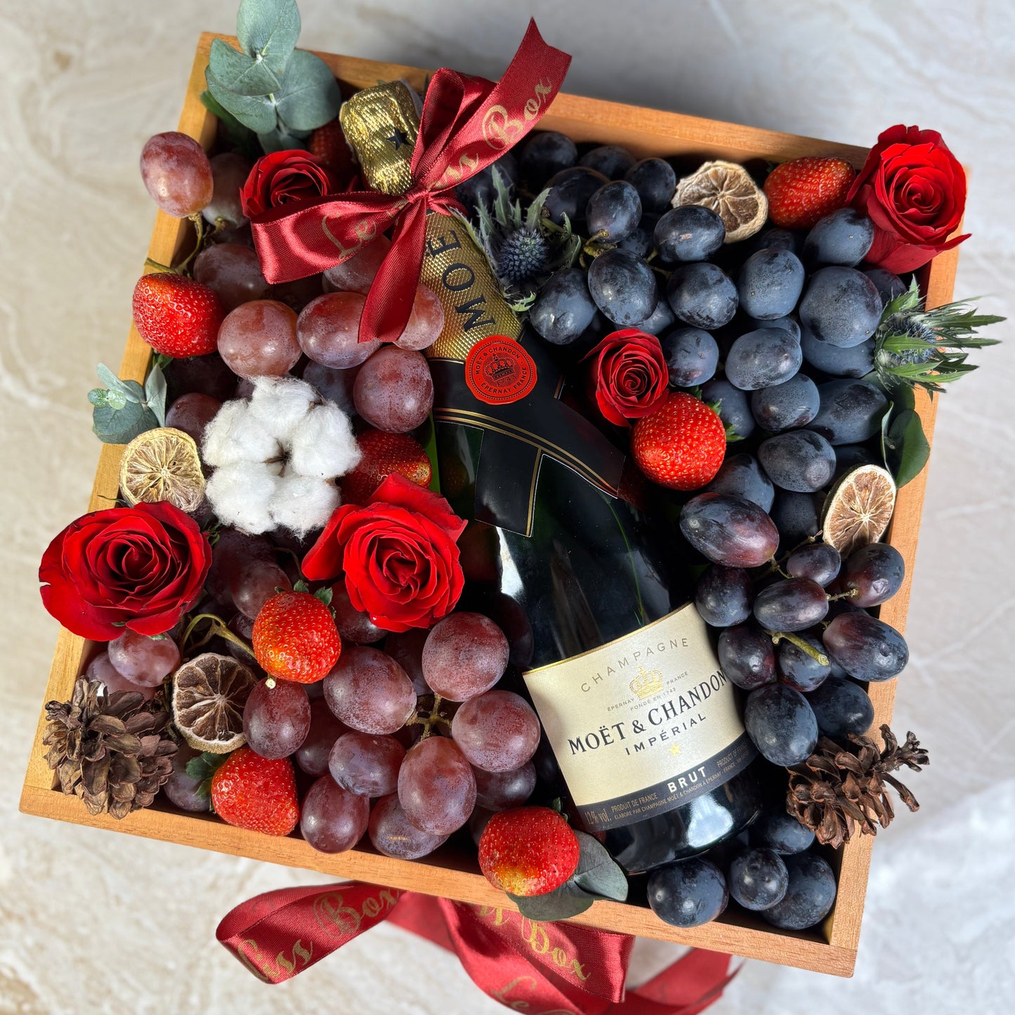 Gift basket with fruits, flowers, and a bottle of Moët & Chandon champagne on a marble surface. moet hamper jakarta, moet hamper surabaya, wine hamper jakarta, champagne hamper jakarta
