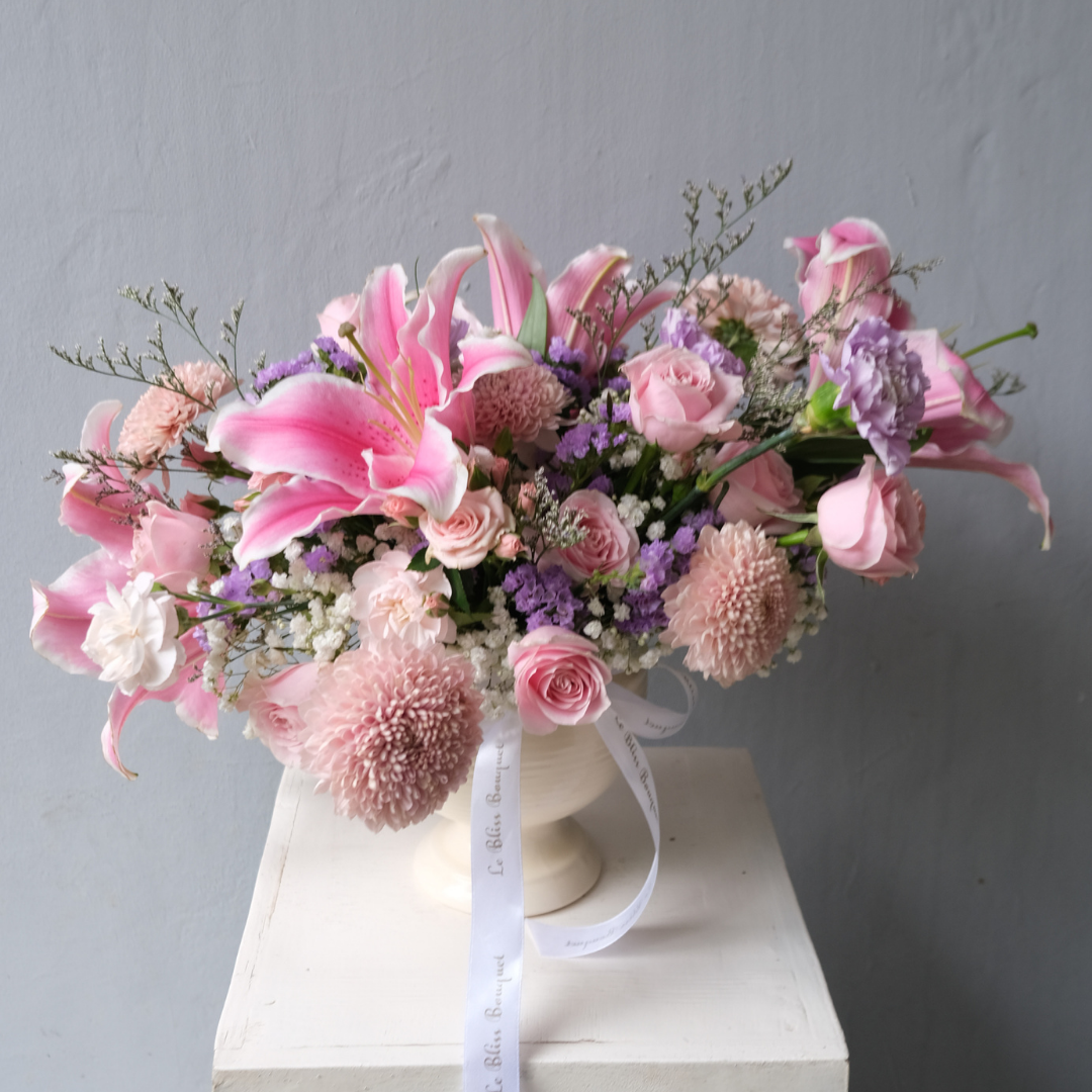 A floral arrangement featuring pink avalanche roses, gompie pink blooms, and lily casablanca in a white vase, set against a neutral background. florist surabaya, toko bunga surabaya, vase arrangement surabaya, sidoarjo, gresik
