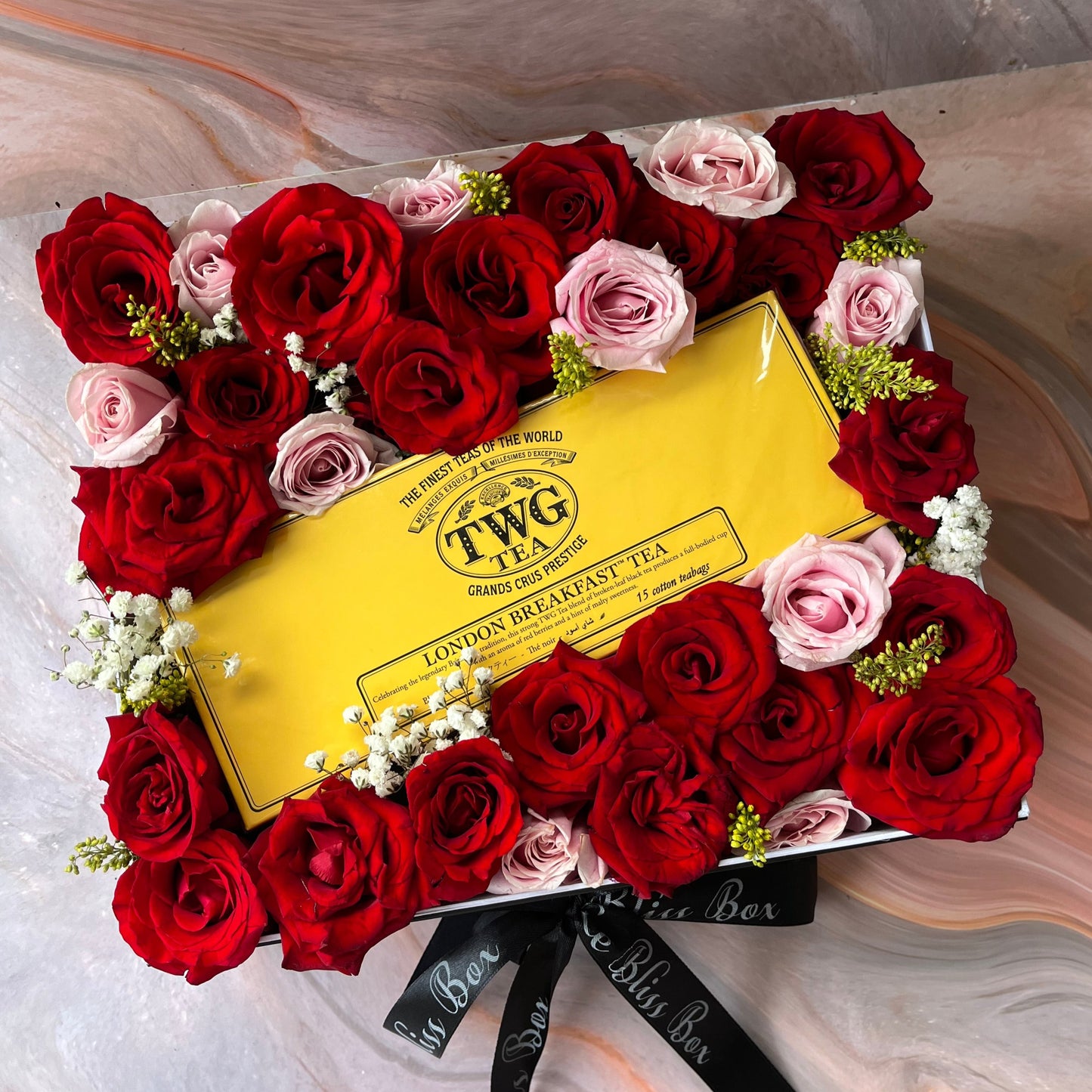 A beautifully arranged rose hamper featuring red and pink roses, with a yellow TWG tea packaging in the center. TWG Hamper jakarta surabaya by le bliss