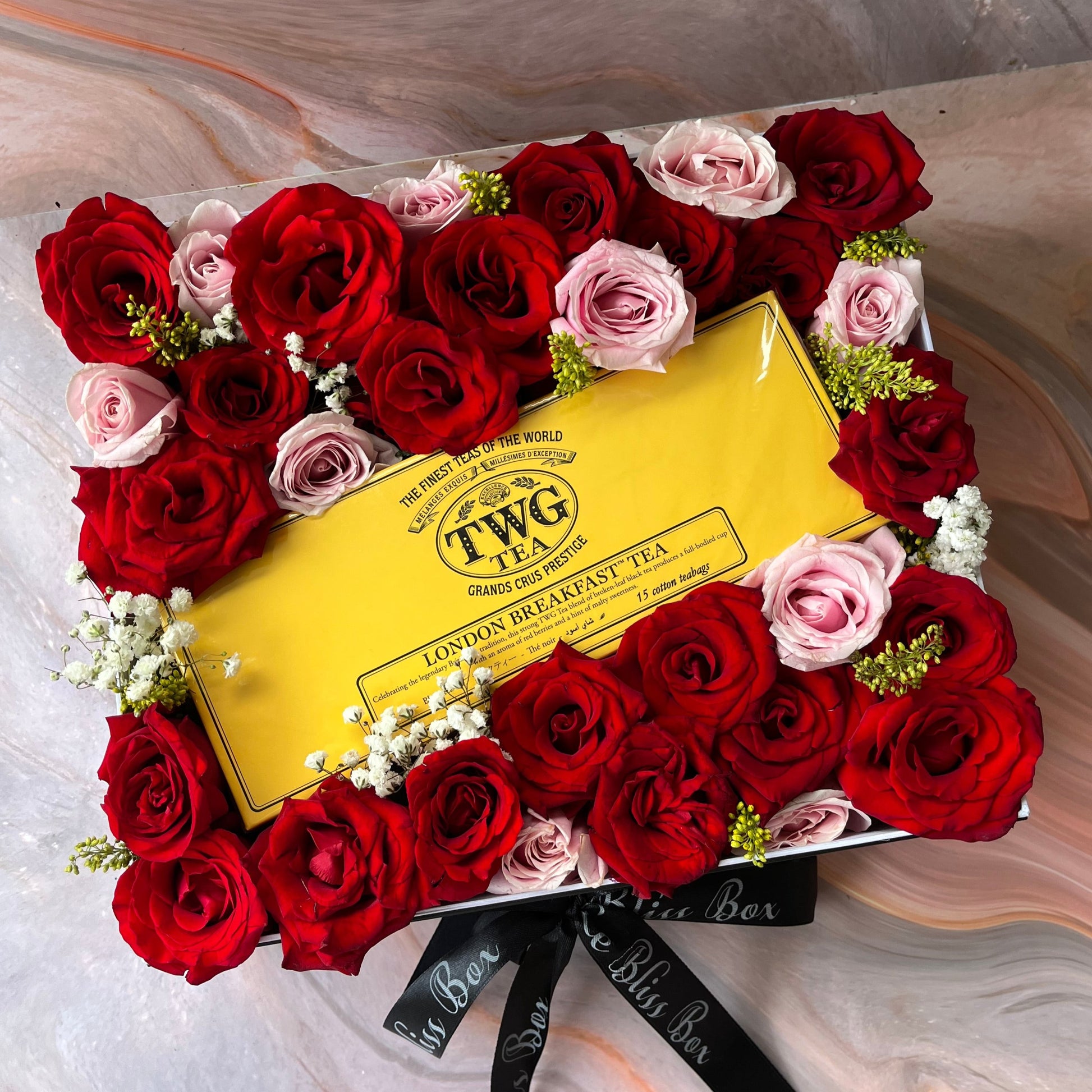 A beautifully arranged rose hamper featuring red and pink roses, with a yellow TWG tea packaging in the center. TWG Hamper jakarta surabaya by le bliss