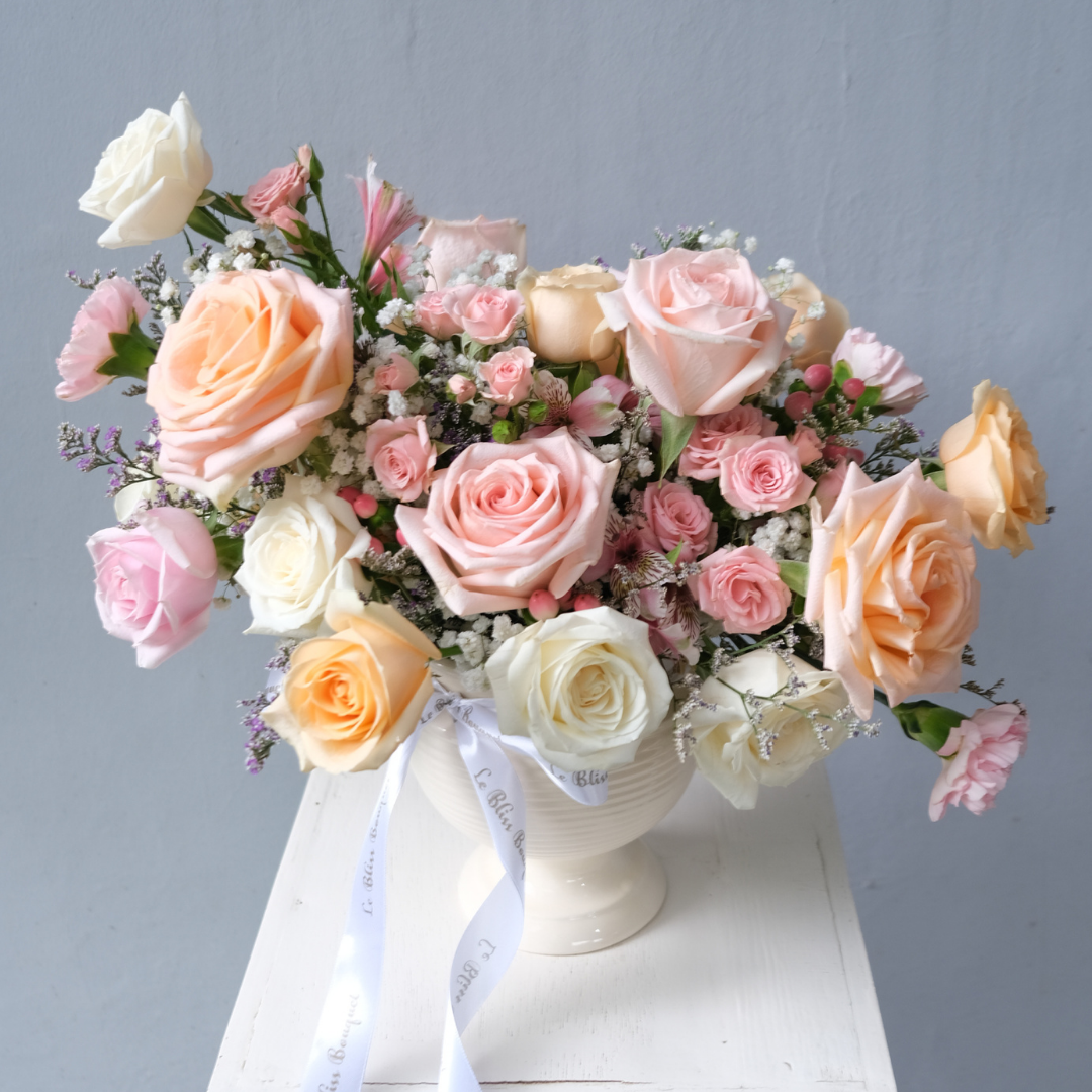 A vase arrangement featuring a mix of pink, peach, and white roses with some greenery in a white vase placed on a white surface. florist Surabaya, rangkaian vas surabaya, jakarta, gresik, sidoarjo