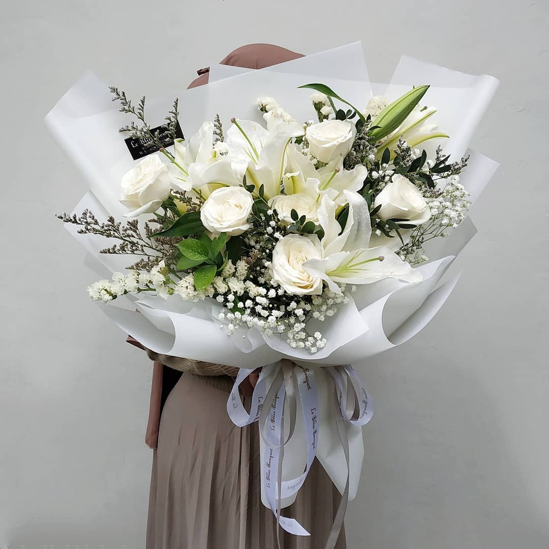 A large bouquet of white flowers with green leaves, wrapped in white paper and tied with a ribbon. flower bouquet surabaya, buket bunga surabaya, jakarta, florist jakarta, bouquet jakarta