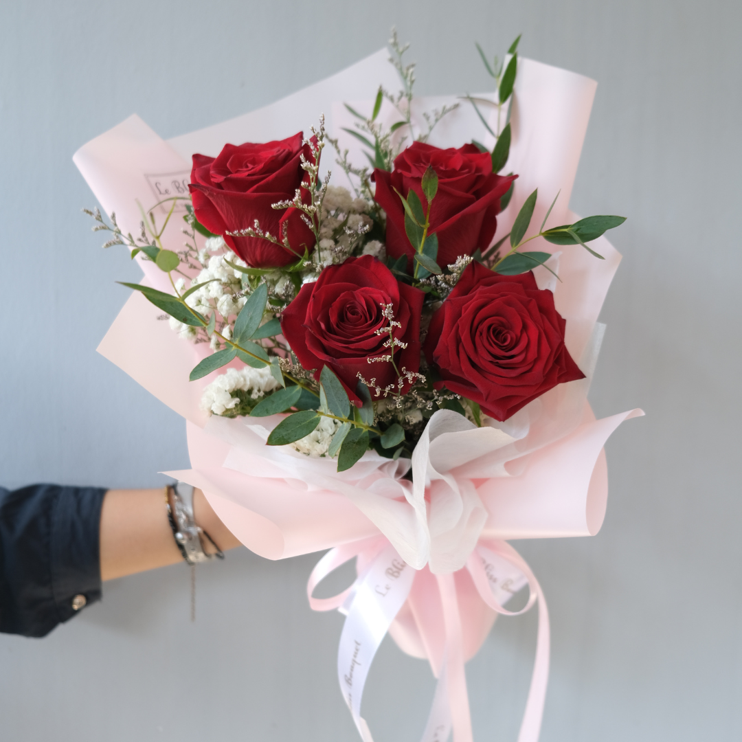 A small bouquet of red explorer roses with green leaves, wrapped in pink and white paper, held by a hand. florist jakarta, florist surabaya, bouquet surabaya