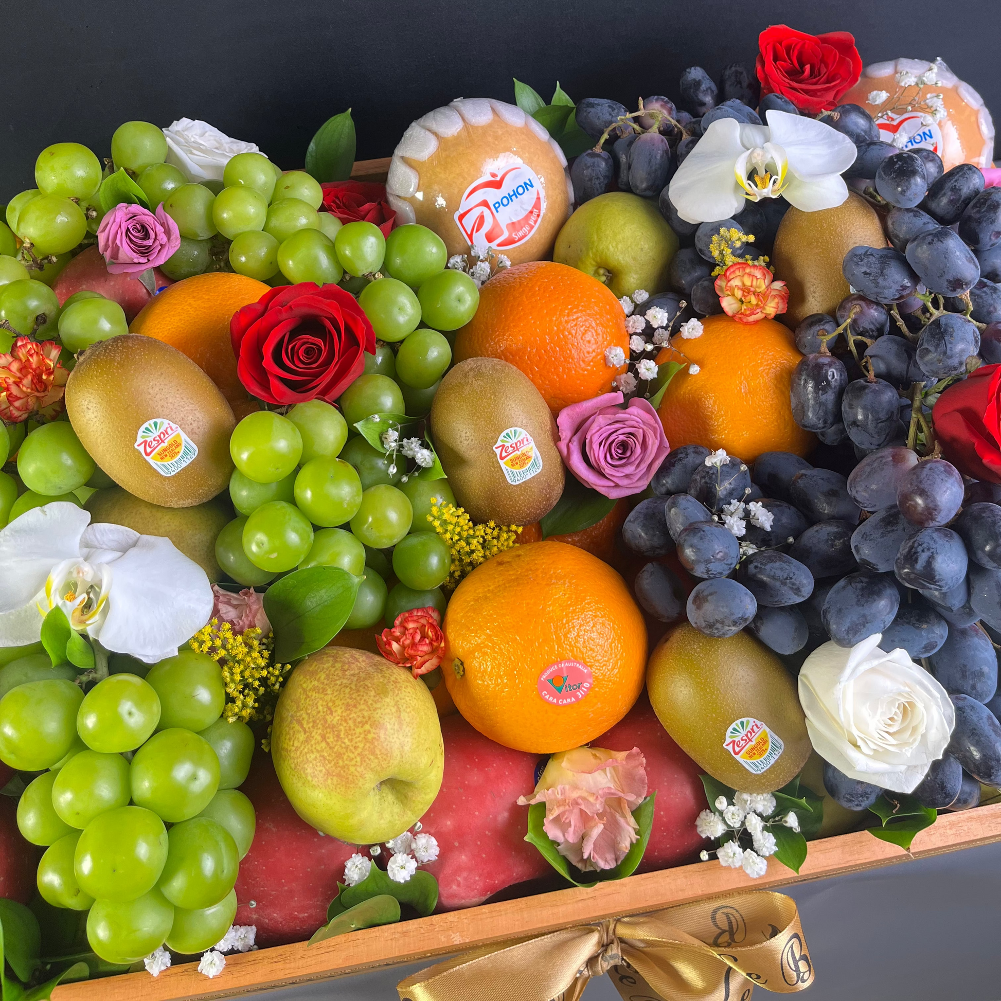 Assorted fruits and flowers arranged in a decorative box on a dark background. parcel buah premium jakarta, tangerang, depok, bekasi, surabaya, gresik, cirebon