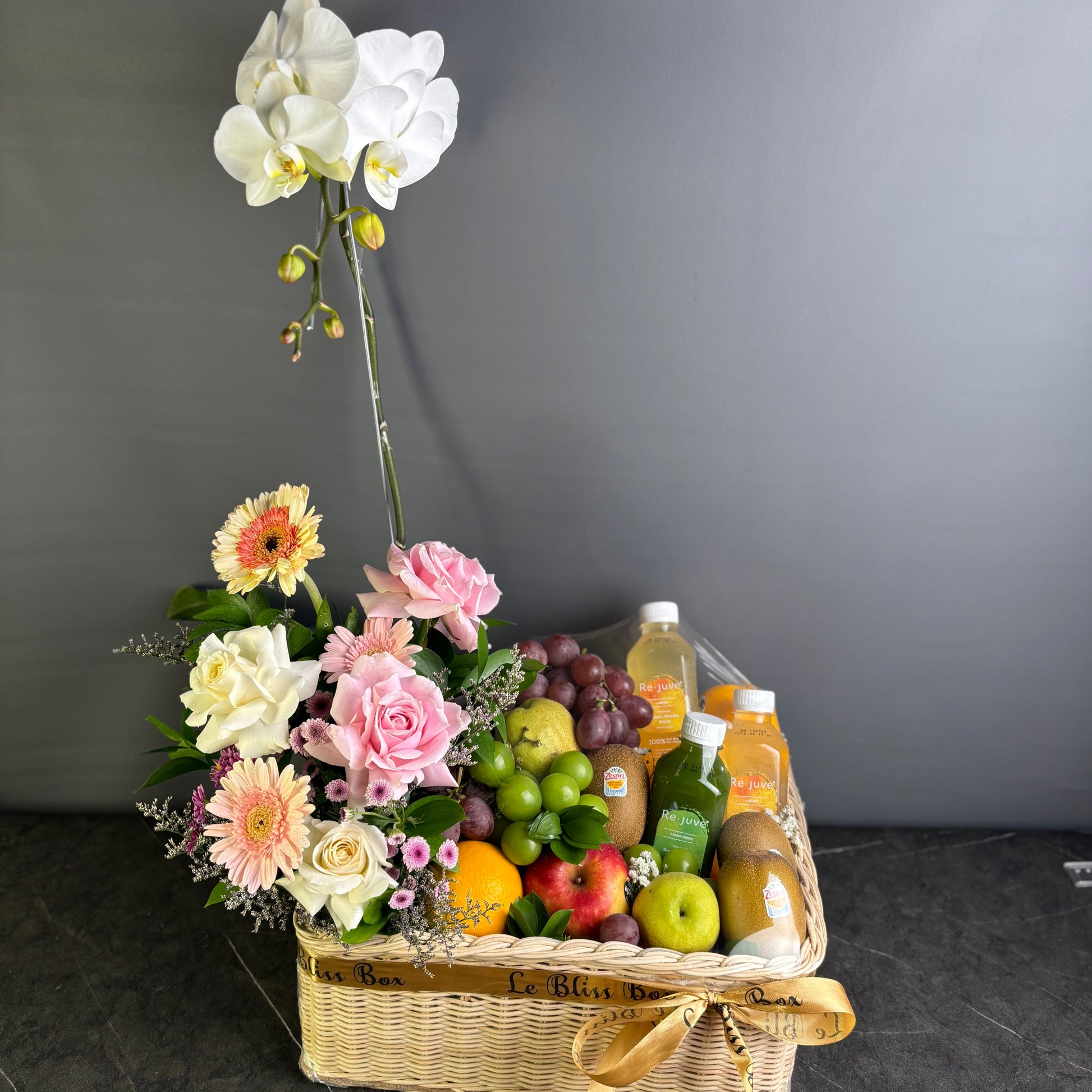 Basket of flowers and fruits on a dark surface with a gray background. parcel buah bunga anggrek dengan rejuve juice hamper by le bliss box. Jakarta, Surabaya, cirebon delivery