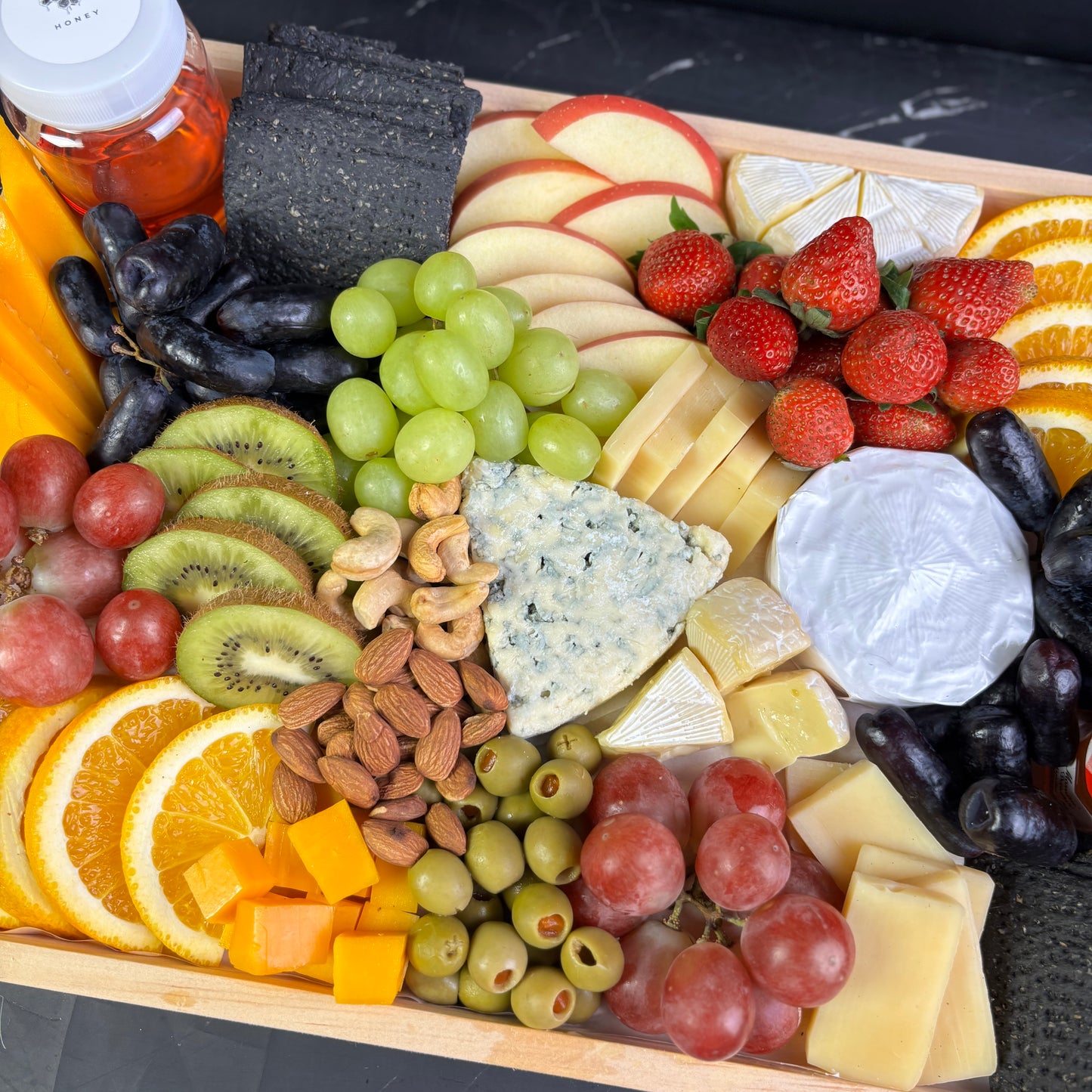 Blue cheese platter with wheat crackers, fresh fruit, and nuts on a wooden charcuterie board, ready for delivery in Jakarta
