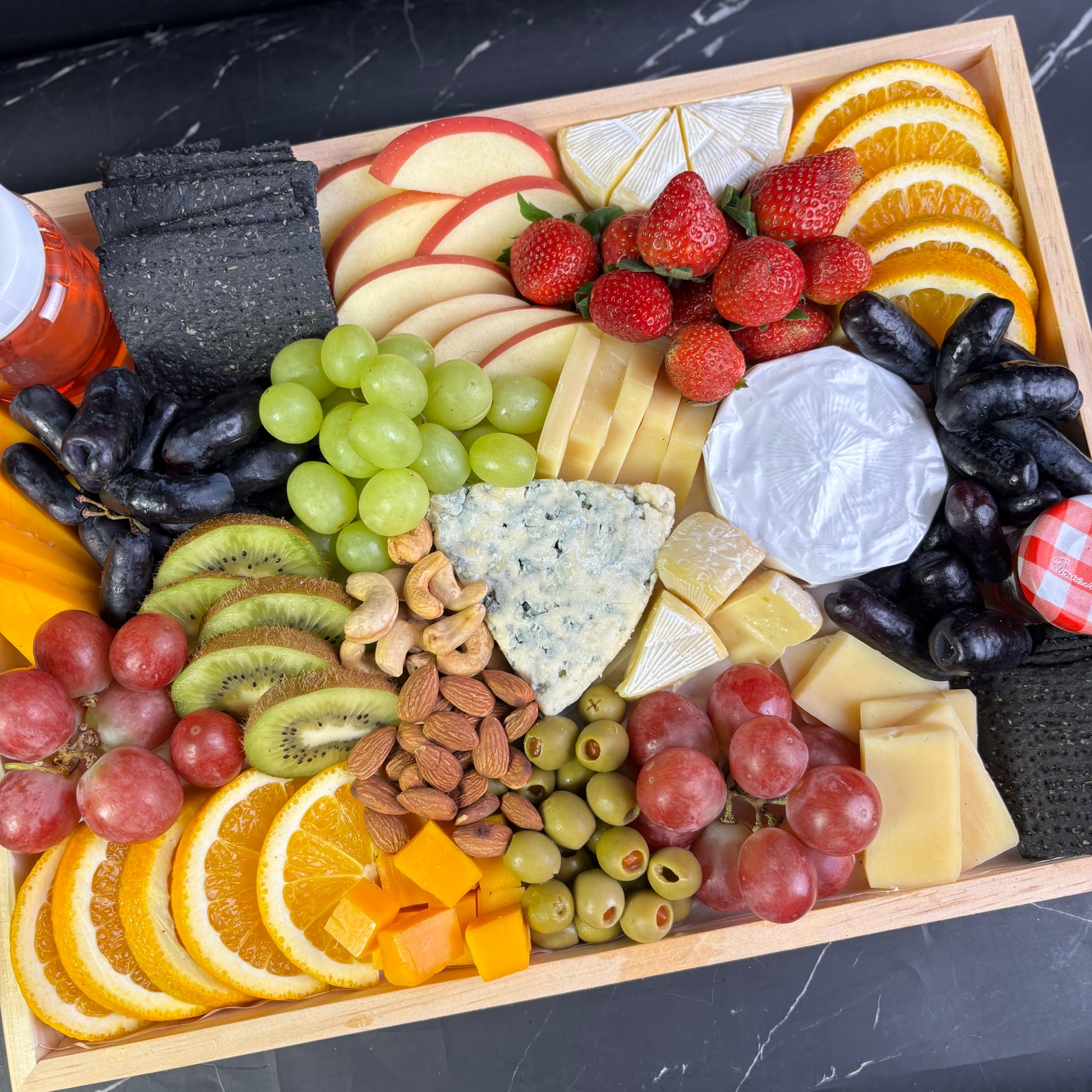 Blue cheese platter with wheat crackers, fresh fruit, and nuts on a wooden charcuterie board, ready for delivery in Surabaya