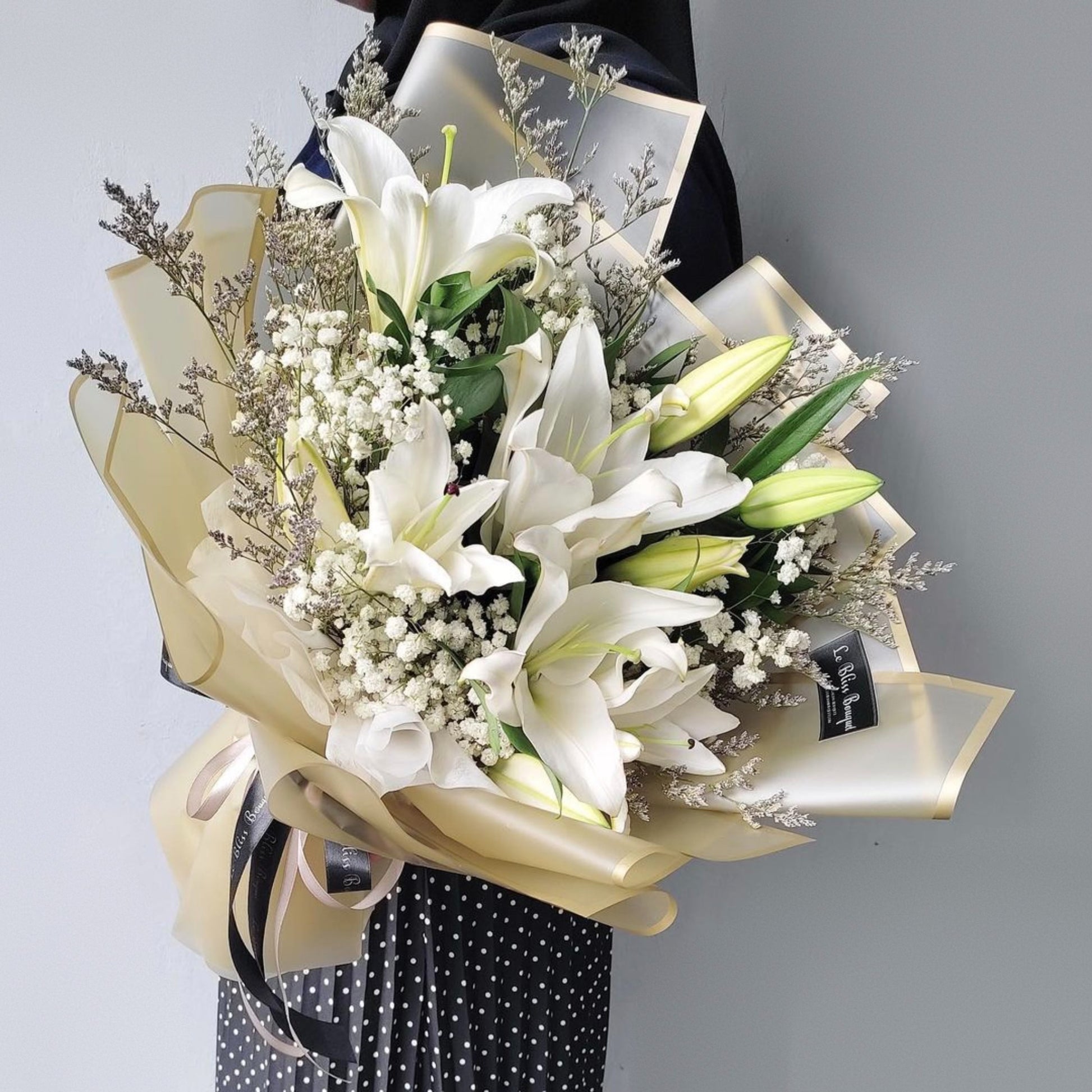 Bouquet of white lilies and greenery with a yellow ribbon against a gray background by Le Bliss Bouquet. best florist jakarta, surabaya, cirebon