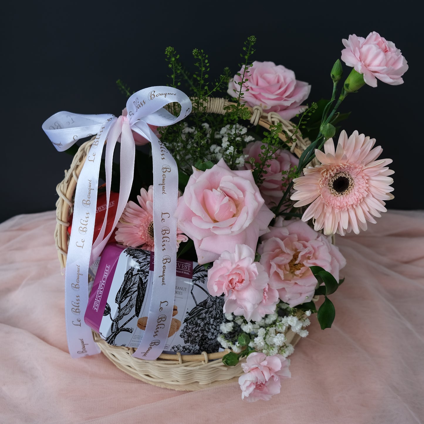 Cookies hamper in rattan basket decorated with a pink flower ring, perfect for gifting. Available for delivery in Jakarta, Bintaro, Tangerang, and Cirebon.
