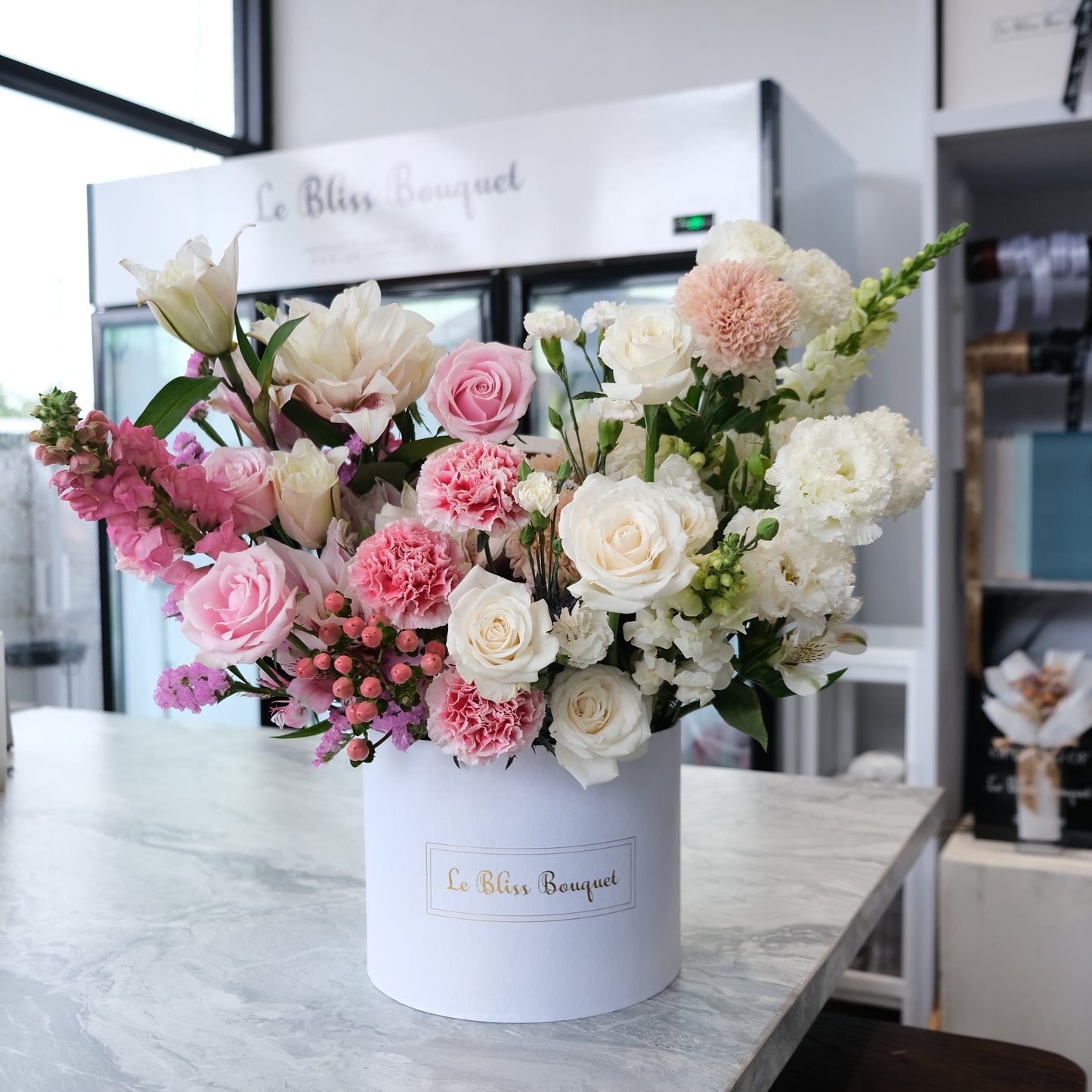A floral arrangement in a white cylindrical container with a mix of pink and white flowers, including roses and carnations, designed by Le Bliss Bouquet. Florist surabaya, florist jakarta