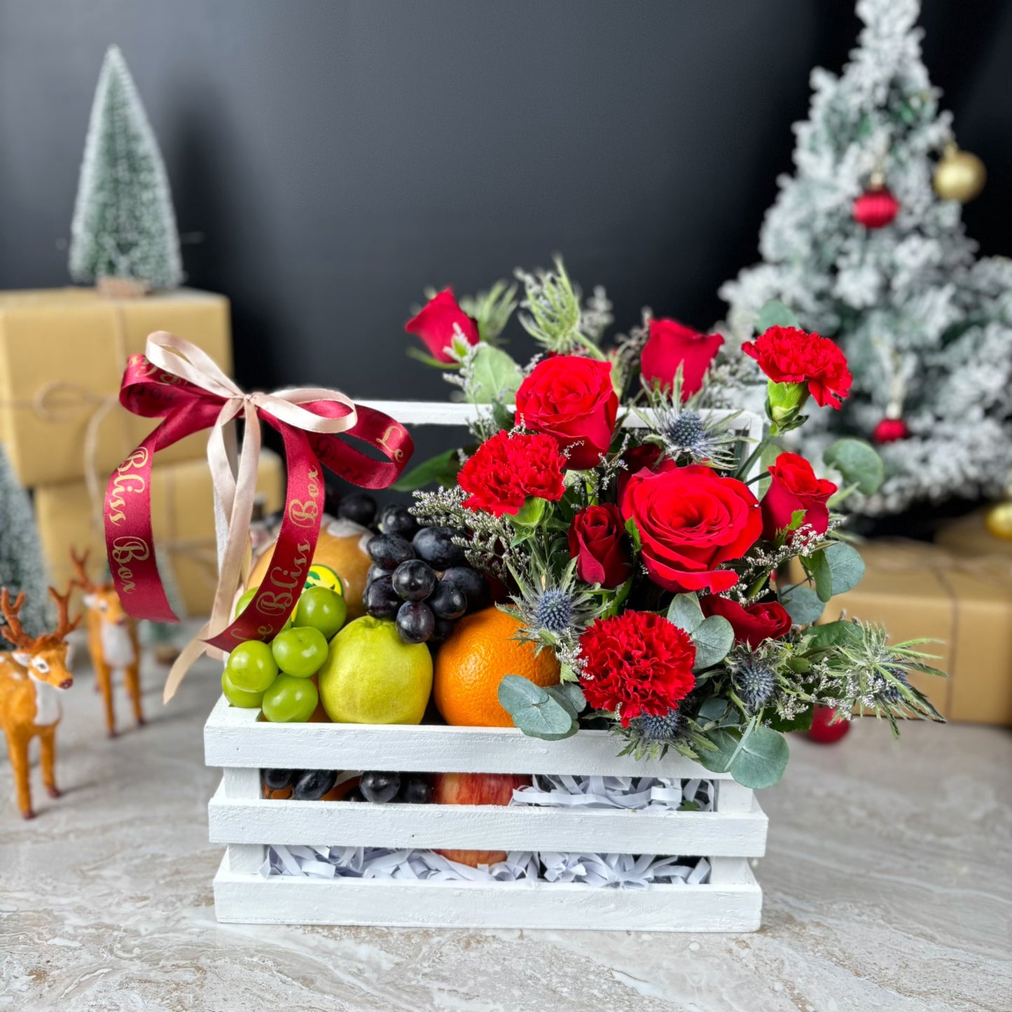 Decorative fruit and flower arrangement in a white crate with Christmas decorations in the background. Blooming Red Crate Fruit Parcel | Best Christmas Hamper in Jakarta & Surabaya – Le Bliss Box