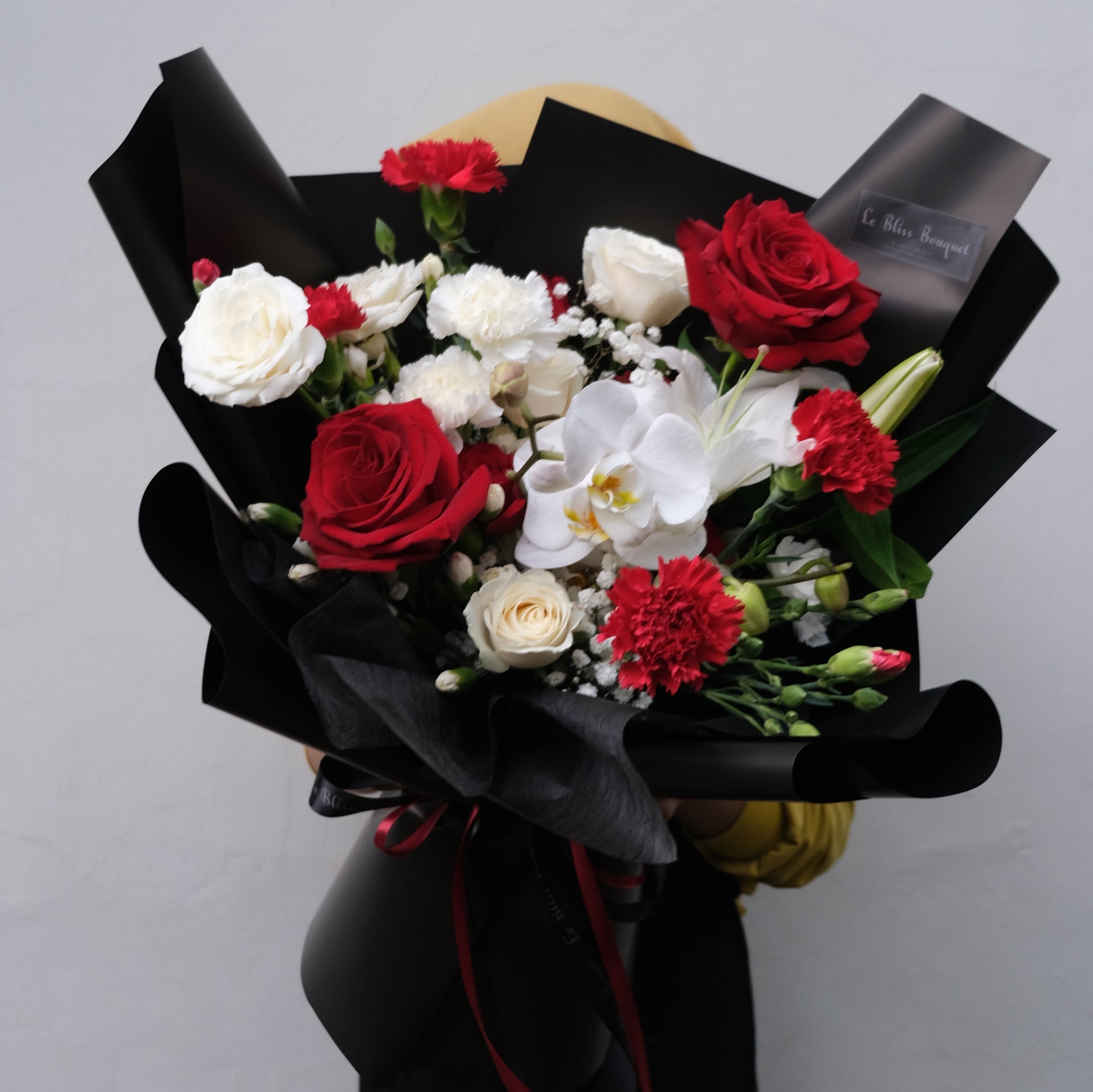 Elegant bouquet featuring red and white roses with white orchids, wrapped in black paper from Le Bliss Bouquet