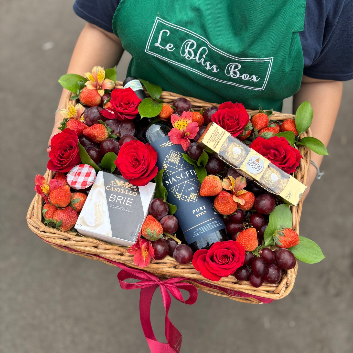 Elegant wine hamper with Sababay Mascetti red wine, Brie cheese, fresh grapes, strawberries, Ferrero Rocher chocolates, and a jam jar, beautifully arranged with fresh flower toppings. Luxury gift hamper for delivery in Jakarta, Bintaro, Tangeran
