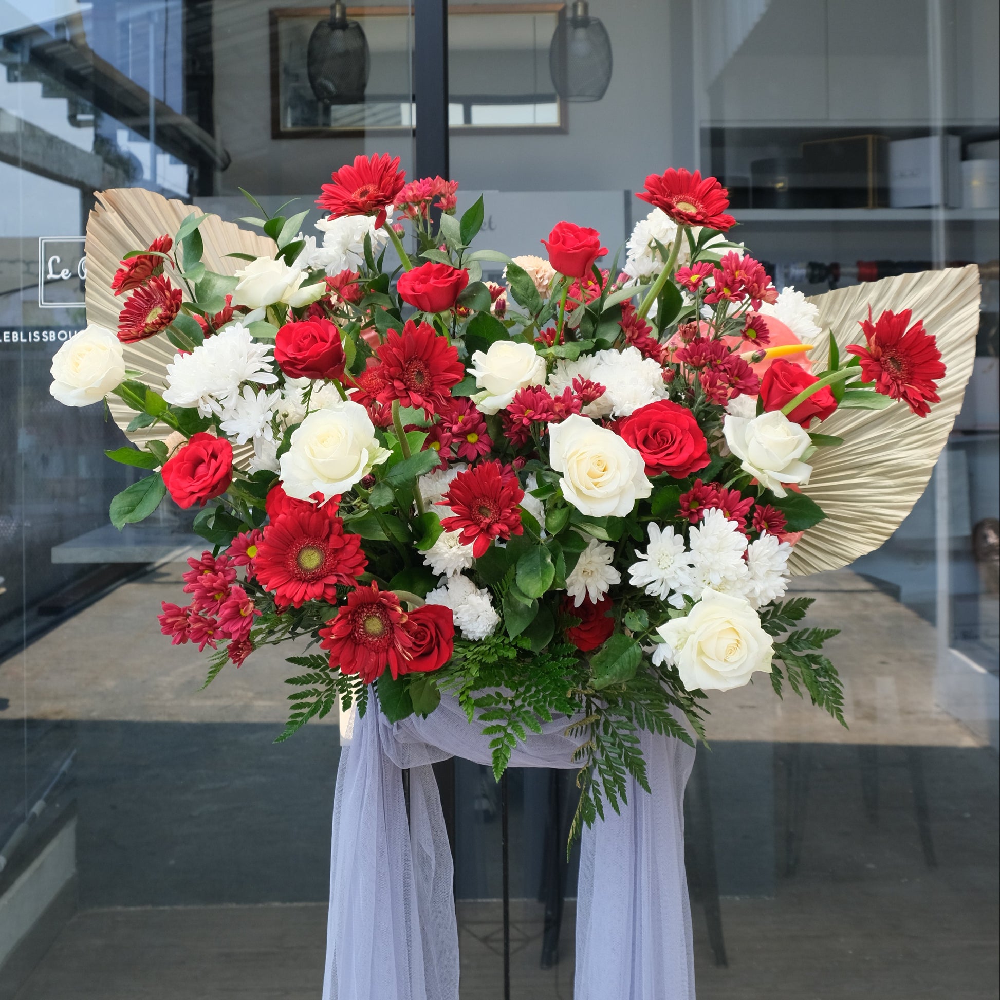 Floral arrangement with red and white flowers in front of a glass door. standing flower surabaya, standing flower cirebon, standing flower bintaro, standing flower jakarta