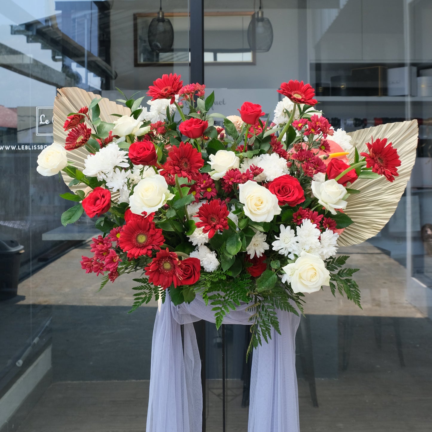 Floral arrangement with red and white flowers on a glass door. Floral arrangement with red and white flowers on a stand in front of a glass door. Elegant Red and White Floral Stand by Le Bliss Bouquet Standing flower jakarta, standing flower surabaya, standing flower cirebon
