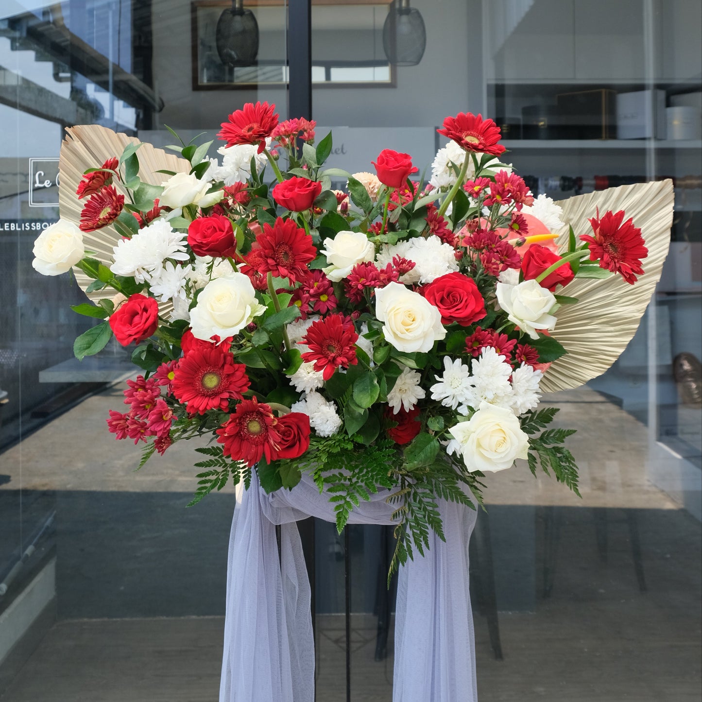 Floral arrangement with red and white flowers on a stand in front of a glass door. Elegant Red and White Floral Stand by Le Bliss Bouquet Standing flower jakarta, standing flower surabaya, standing flower cirebon