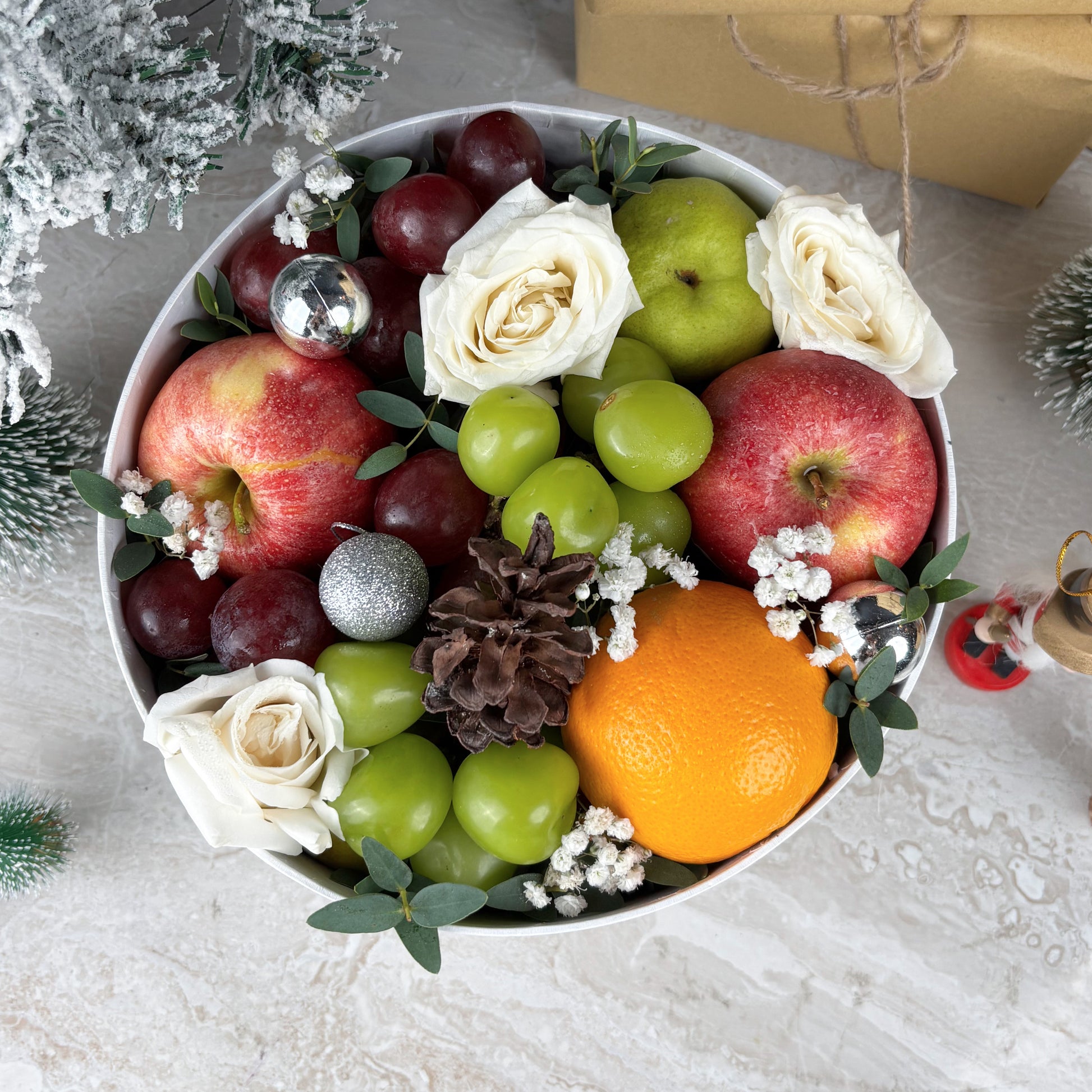 Fruit and flower arrangement in a bowl on a festive background. Winter Sonata Round Fruit Box dari Le Bliss Box. Christmas fruit hamper elegan dengan buah premium. Pengiriman Surabaya, Jakarta & Cirebon. Luxury, festive, and fresh.