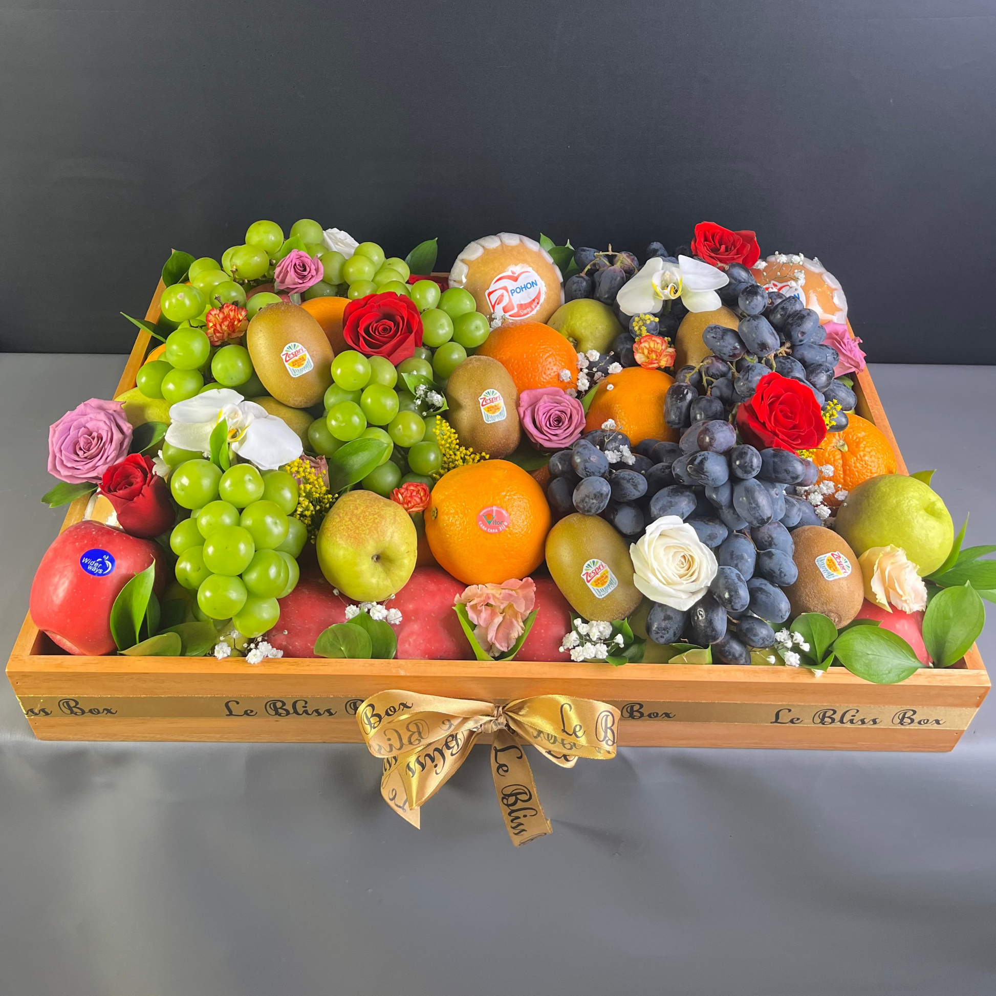 Fruit arrangement in a wooden box on a gray background. Assorted fruits and flowers arranged in a decorative box on a dark background. parcel buah premium jakarta, tangerang, depok, bekasi, surabaya, gresik, cirebon