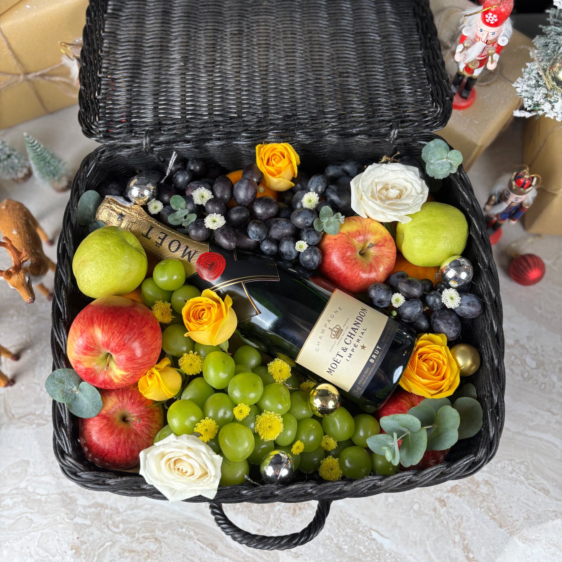 Fruit basket with moet champagne bottle, apples, grapes, and flowers on a textured surface. Midnight Moët Champagne Hamper | Best Christmas Hamper in Jakarta, Surabaya & Tangerang – Le Bliss Box
