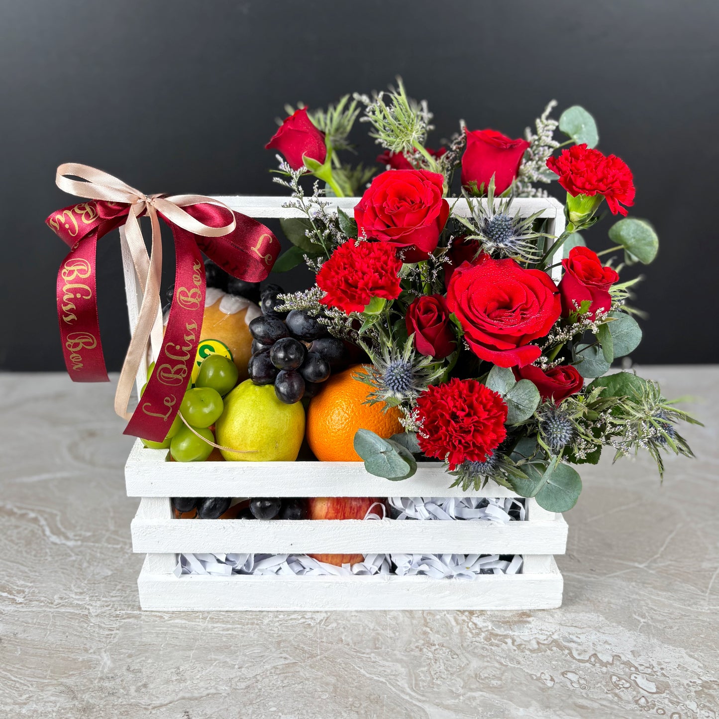 Fruit basket with red roses and a decorative ribbon on a dark background. parcel buah natal surabaya, parcel buah natal jakarta, parcel buah natal cirebon by le bliss box