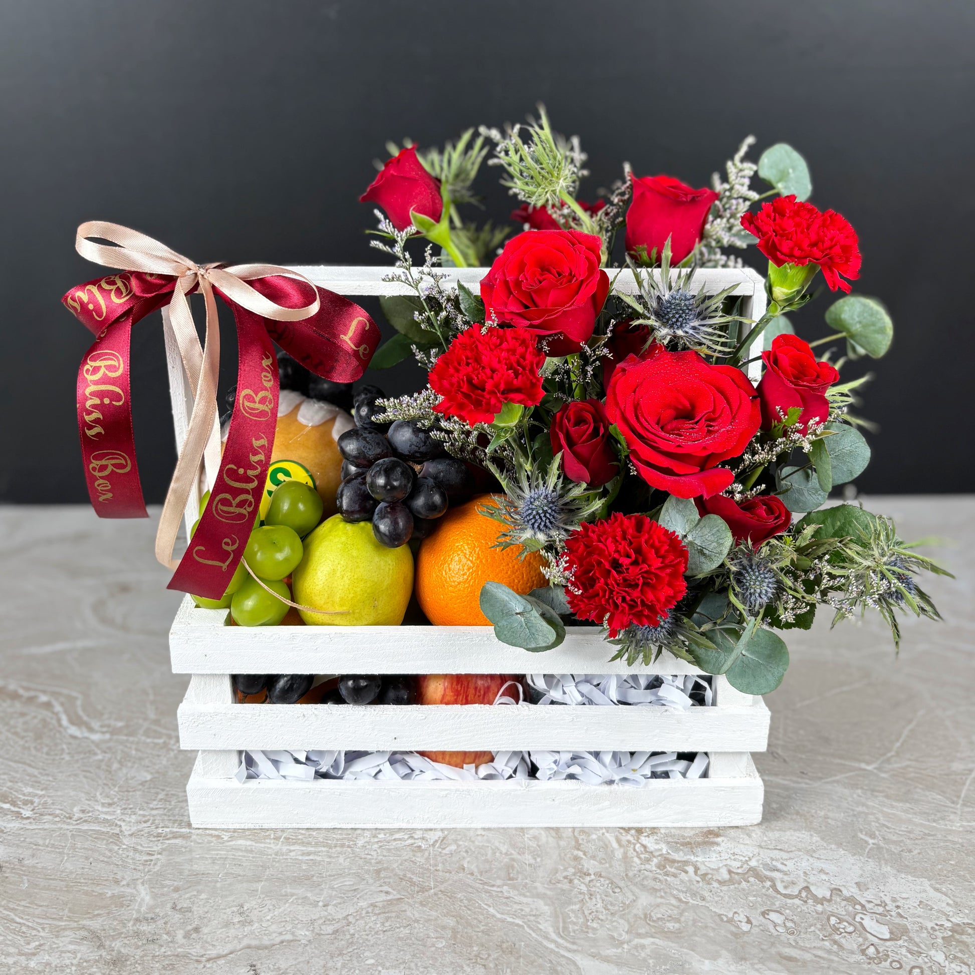 Fruit basket with red roses and a decorative ribbon on a dark background. parcel buah natal surabaya, parcel buah natal jakarta, parcel buah natal cirebon by le bliss box