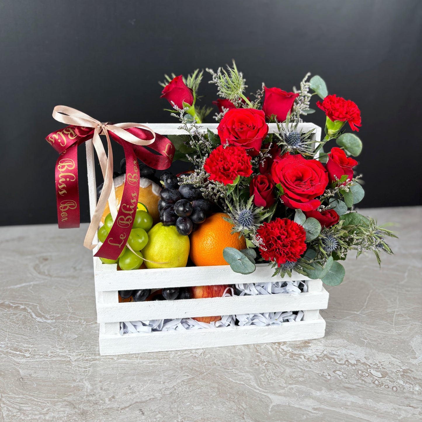 Fruit basket with red roses and a decorative ribbon on a gray surface. Fruit basket with red roses and a decorative ribbon on a dark background. parcel buah natal surabaya, parcel buah natal jakarta, parcel buah natal cirebon by le bliss box