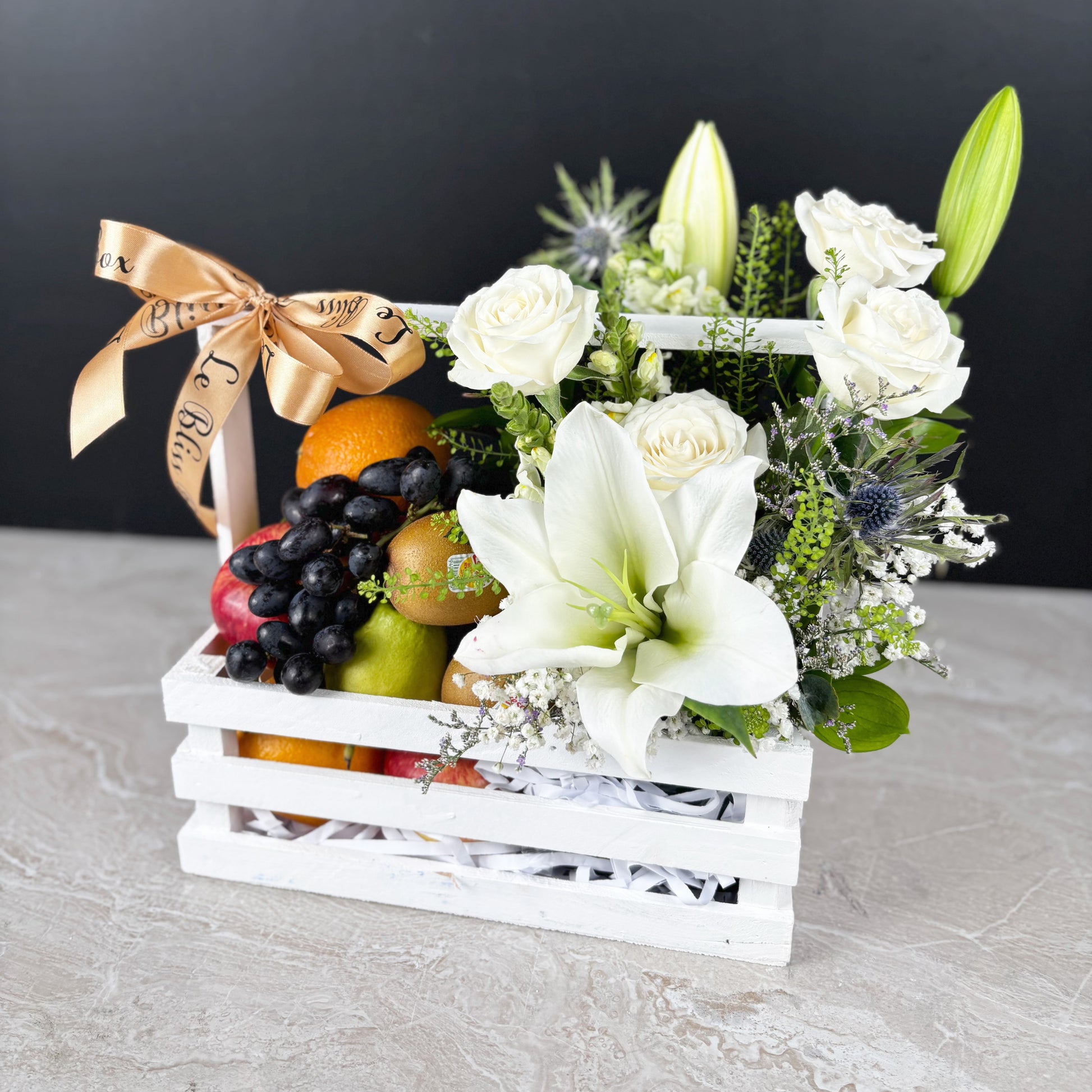 Fruit basket with white flowers and a decorative bow on a gray surface by le bliss box. best fruit parcel in jakarta, surabaya, cirebon