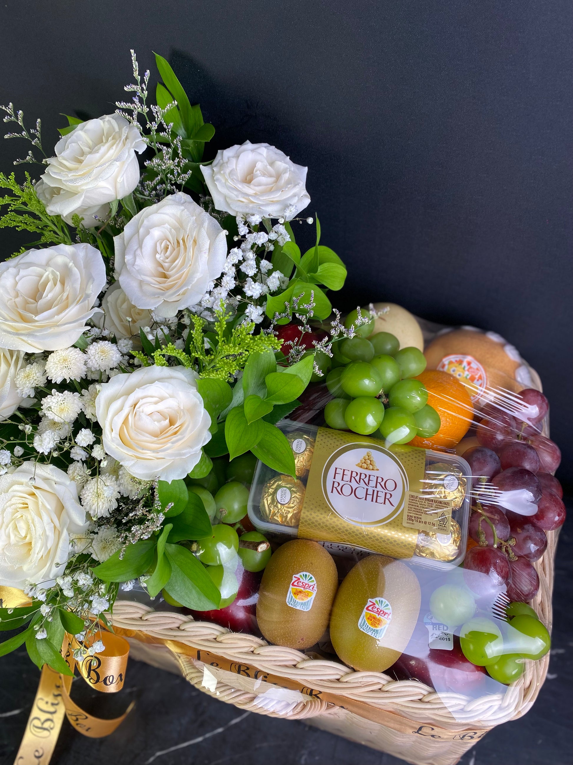 Fruit basket with white roses and a gold ribbon on a dark background. Florist Le Bliss Box parcel buah surabaya, parcel buah jakarta, coklat parcel buah surabaya