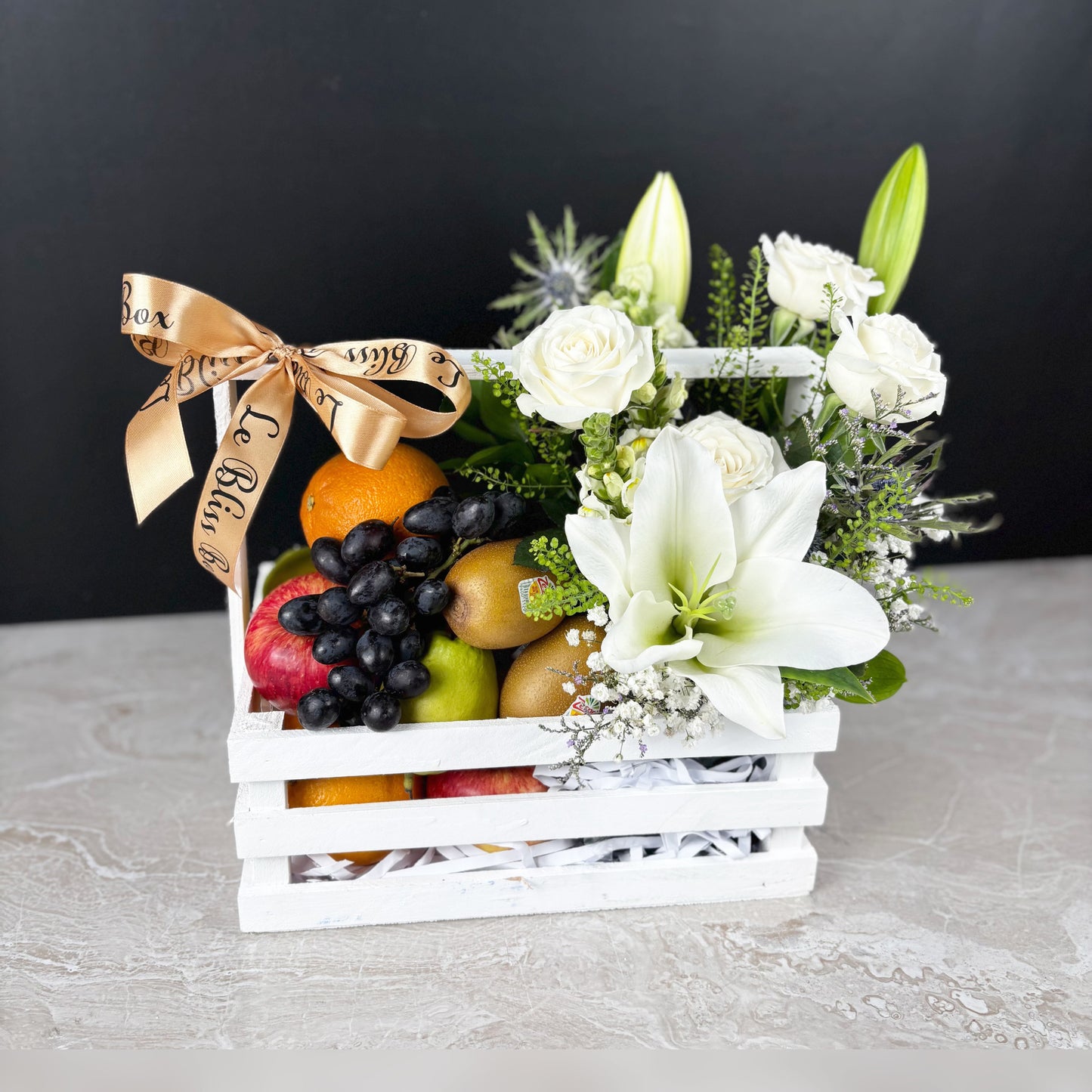Fruit hamper with white flowers and a decorative bow on a gray surface by le bliss box. best fruit parcel in jakarta, surabaya, cirebon