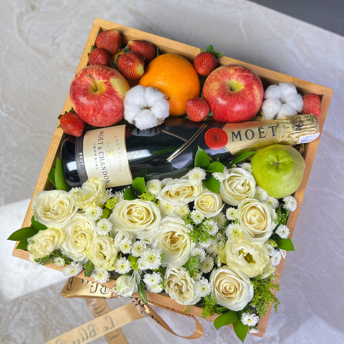 Gift basket with flowers, fruits, and a bottle of Moët champagne on a marble surface. Wine hamper jakarta, wine hamper surabaya, tangerang, depok, bekasi, bogor by le bliss