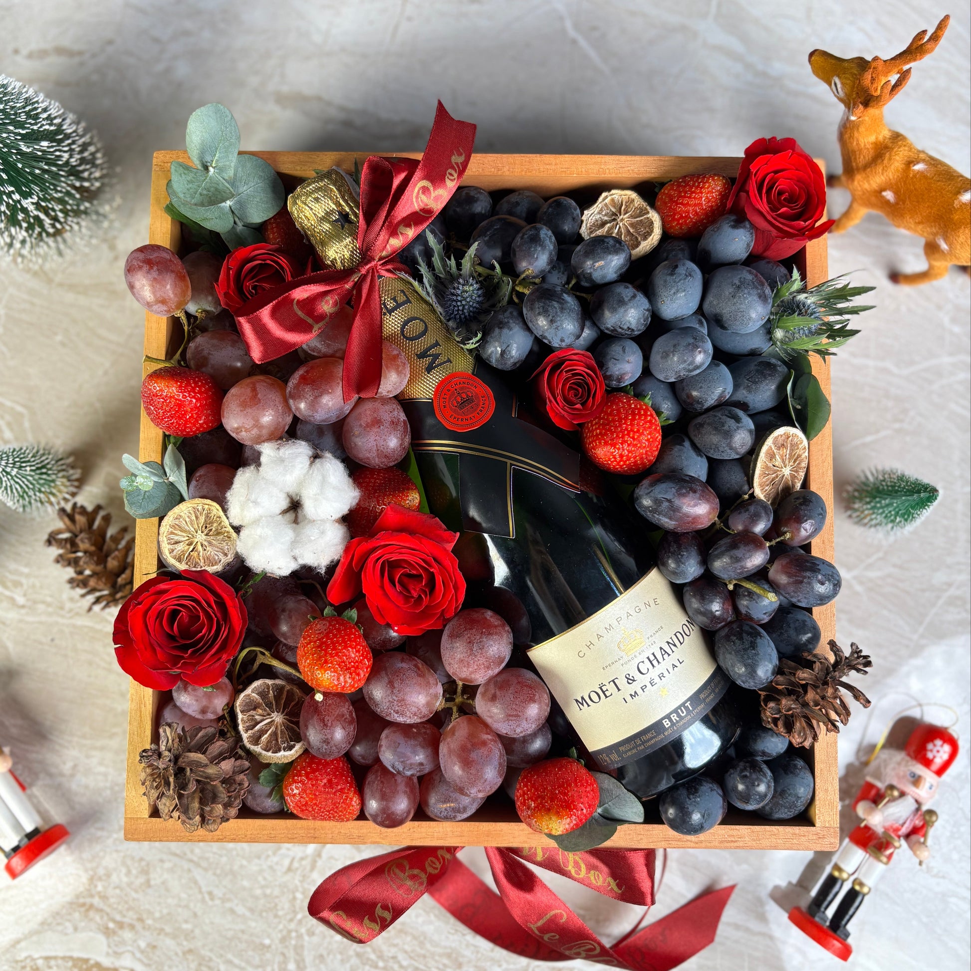 Gift box with champagne, grapes, and flowers on a marble surface. Moet Fruit Hamper by Le Bliss Box, moet hamper jakarta, moet hamper surabaya, wine hamper jakarta, champagne hamper jakarta