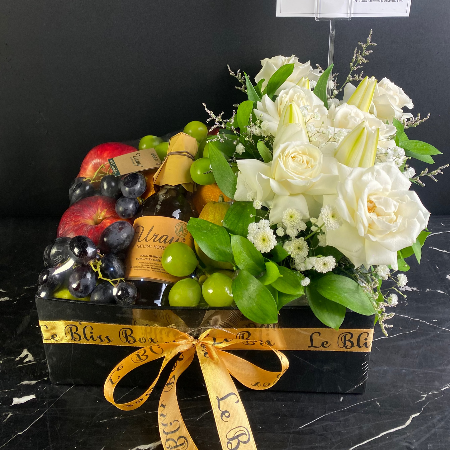Gift box with fruits, wine, and flowers on a dark surface. honey fruit box, fruit hamper with fresh roses, lily and honey. parcel buah surabaya, gresik, jakarta, sidoarjo, tangerang