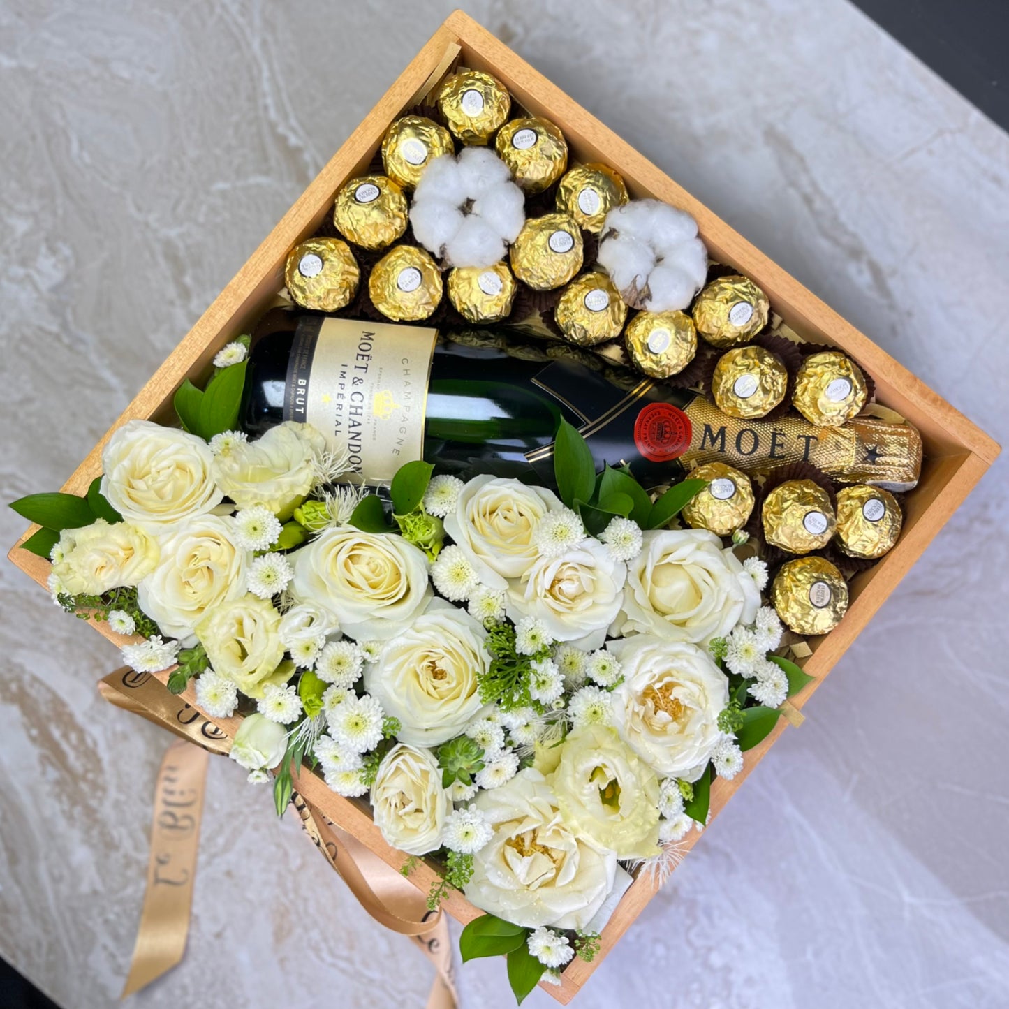 Gift box with white flowers, chocolates, and a bottle of champagne on a light background. Wine hamper jakarta, surabaya, tangerang by le bliss