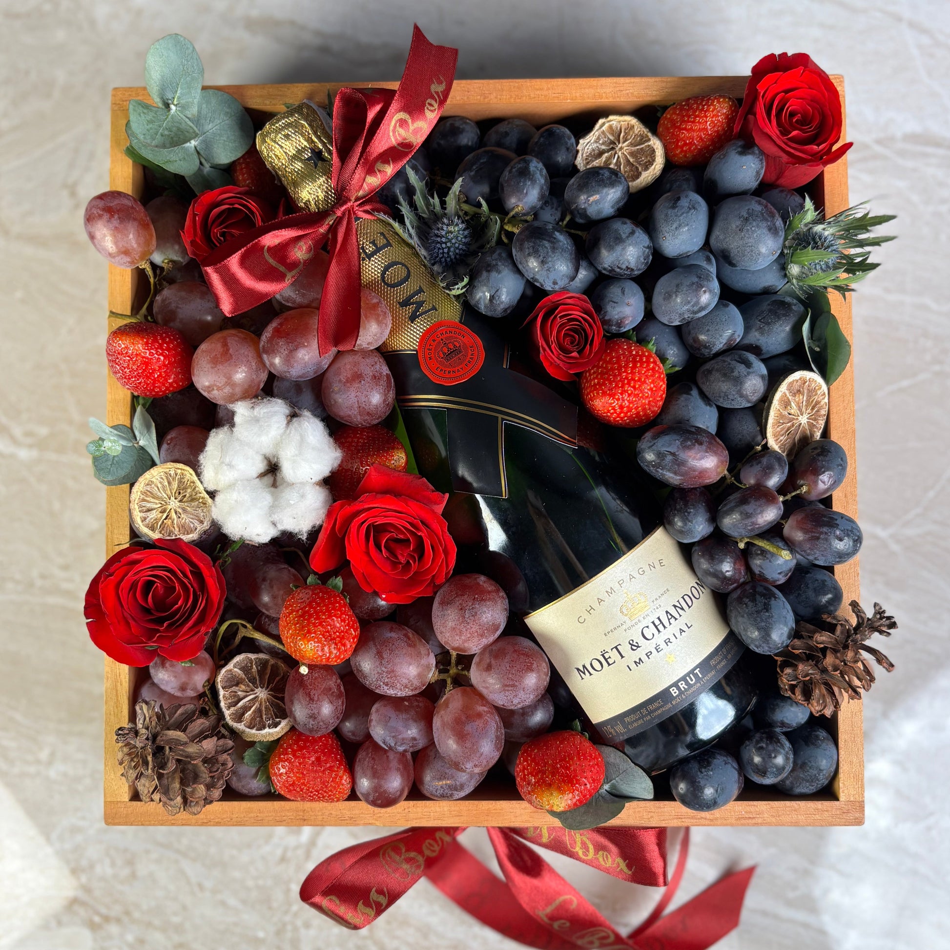 Gift box with wine, fruits, and flowers on a marble surface. Moet Fruit Hamper by Le Bliss Box, moet hamper jakarta, moet hamper surabaya, wine hamper jakarta