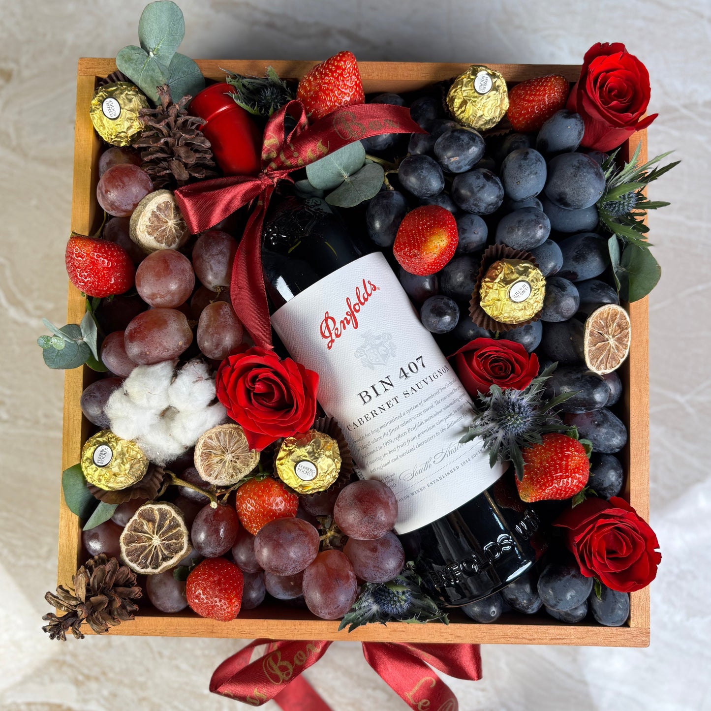 Gift with fruits, flowers, and a bottle of wine on a textured surface. Penfolds Wine Hamper Jakarta, Surabaya. With Fresh autumn grapes, red globe grapes and strawberries and chocolate. Wine Hamper Jakarta. Christmas hamper jakarta