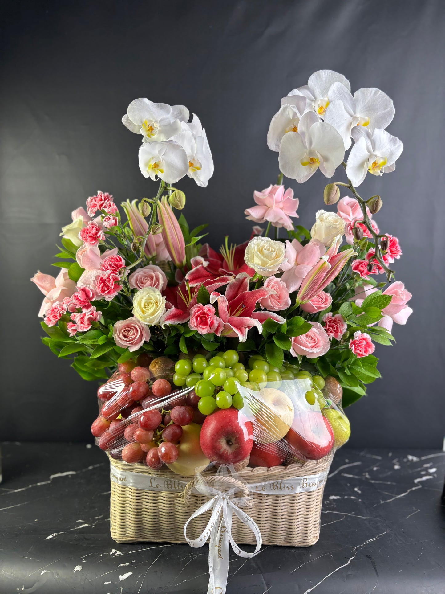Parcel buah premium dengan anggrek pink, berisi buah segar seperti jeruk, apel, dan stroberi dalam keranjang rotan mewah — Grand Pink Orchid Fruit Parcel oleh Le Bliss Surabaya. parcel buah surabaya