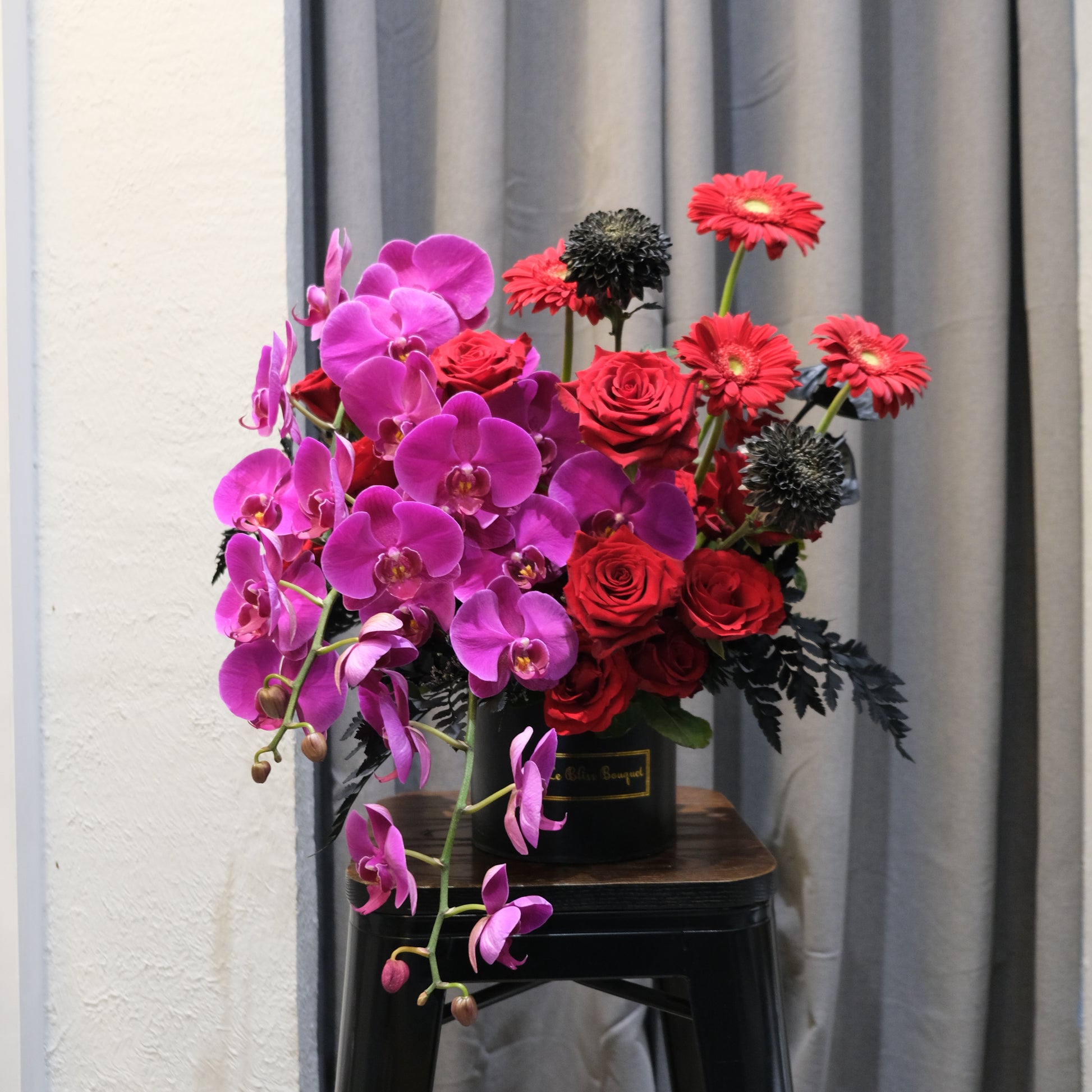 Midnight Orchid Luxe petite bloombox featuring vibrant purple orchids, red explorer roses, and black chrysanthemums in a round black Le Bliss Bouquet box – luxury flower arrangement for delivery in Jakarta