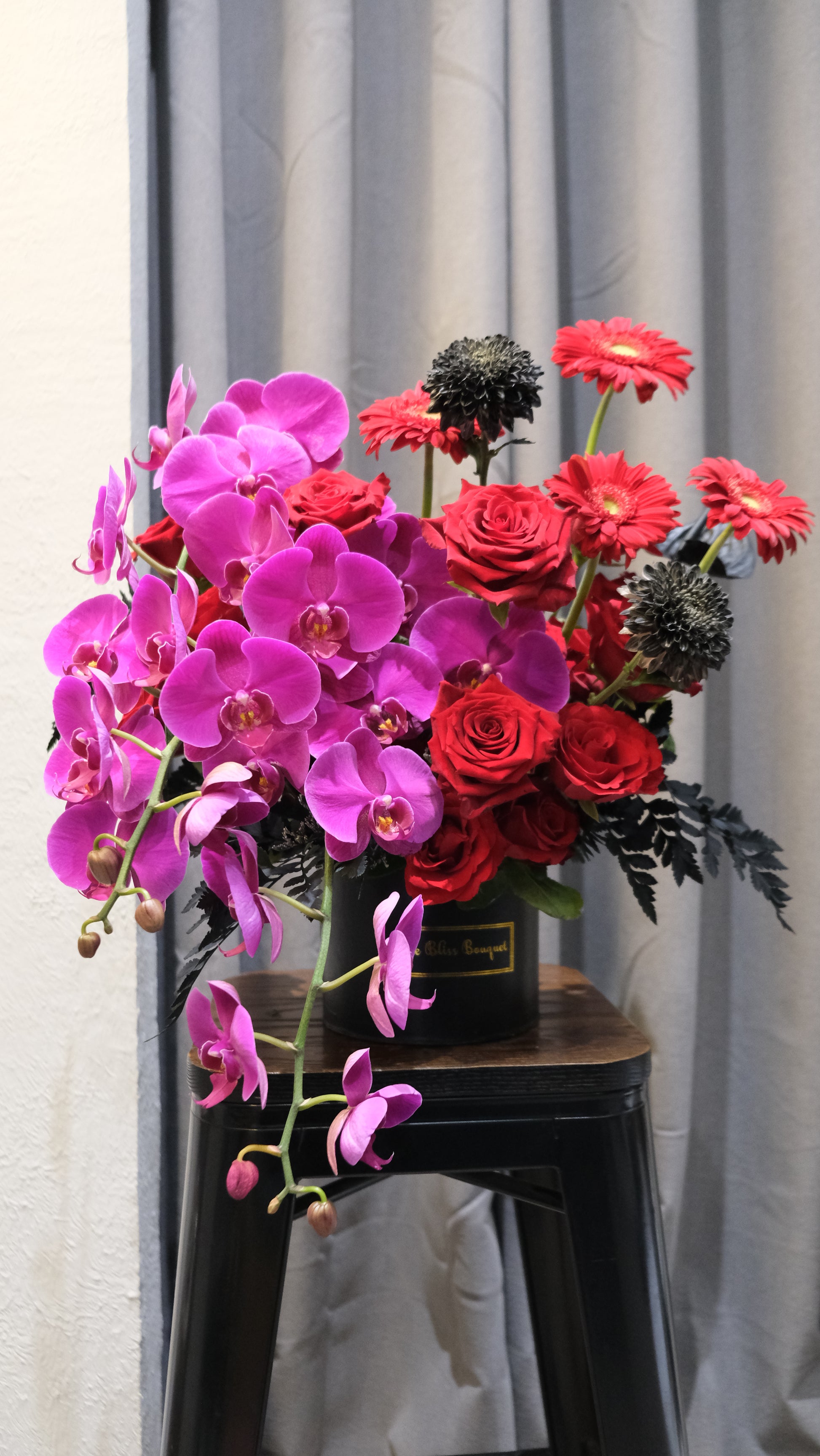 Midnight Orchid Luxe petite bloombox featuring vibrant purple orchids, red explorer roses, and black chrysanthemums in a round black Le Bliss Bouquet box – luxury flower arrangement for delivery in Jakarta Indonesia
