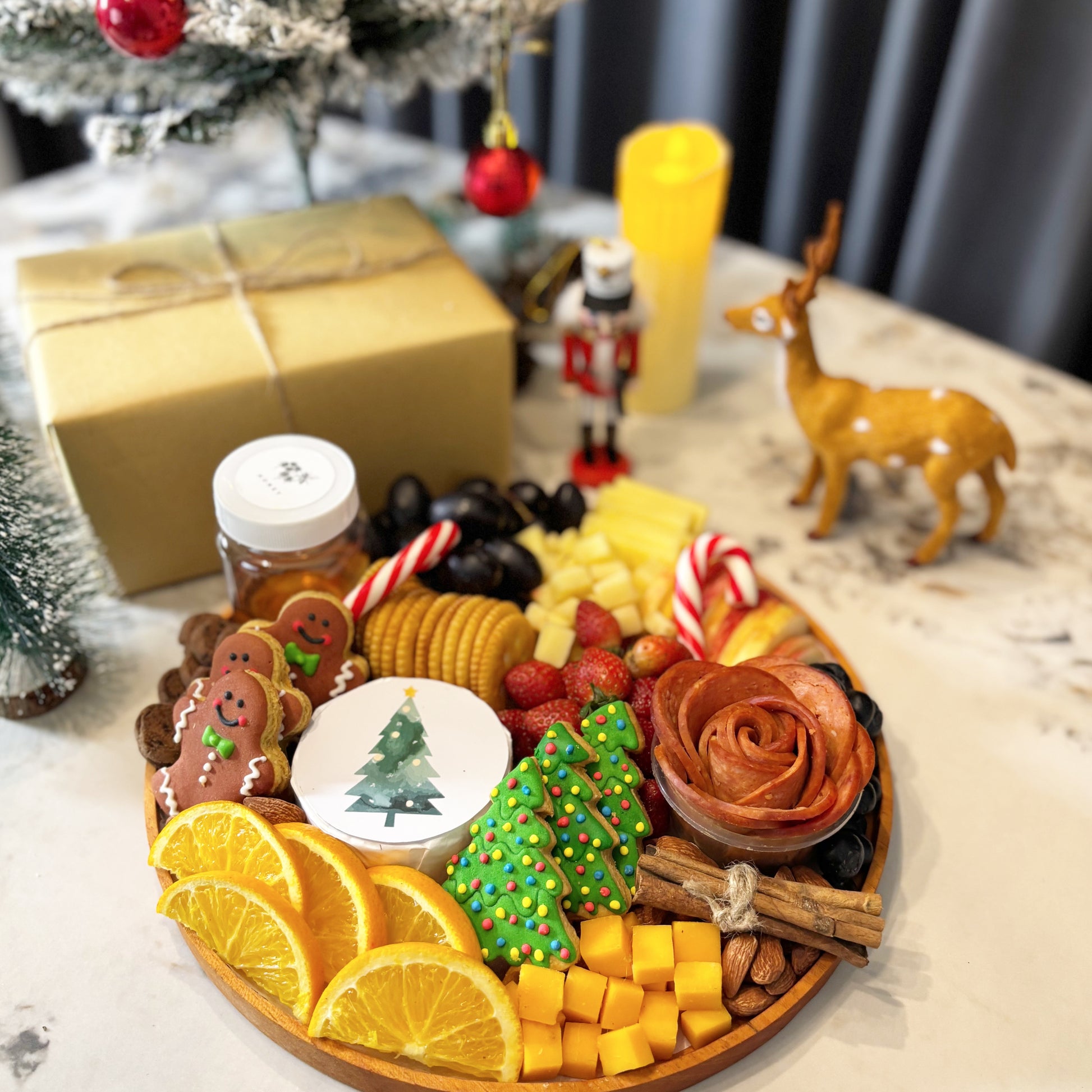 christmas charcuterie board jakarta with fruits, cookies, and a small Christmas tree on a table with festive decorations.  festive charcuterie board with fruits, cheese, and meats on a marble surface. Christmas Round Cheese Platter | Christmas Platter Jakarta & Surabaya – Le Bliss Platter