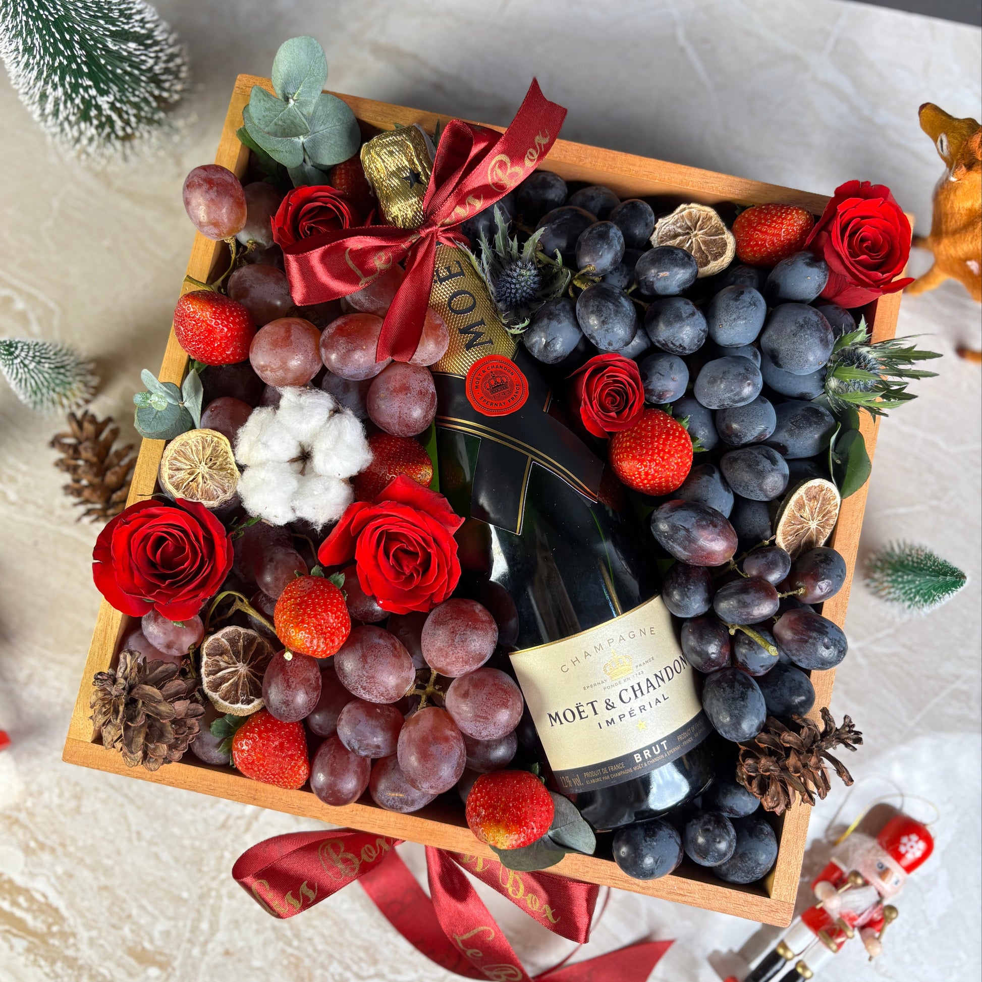 christmas hamper box with champagne, grapes, and flowers on a marble surface. Moet Fruit Hamper by Le Bliss Box, moet hamper jakarta, moet hamper surabaya, wine hamper jakarta, champagne hamper jakarta