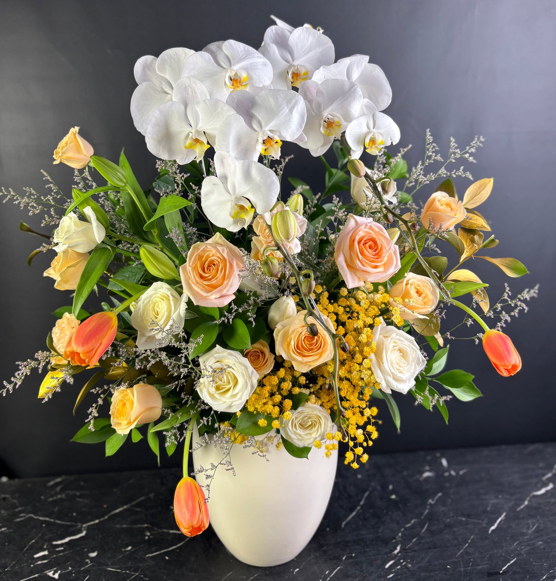 flowers with white orchids, roses, and other flowers in a vase on a dark surface. Florist Jakarta, Surabaya, Cirebon