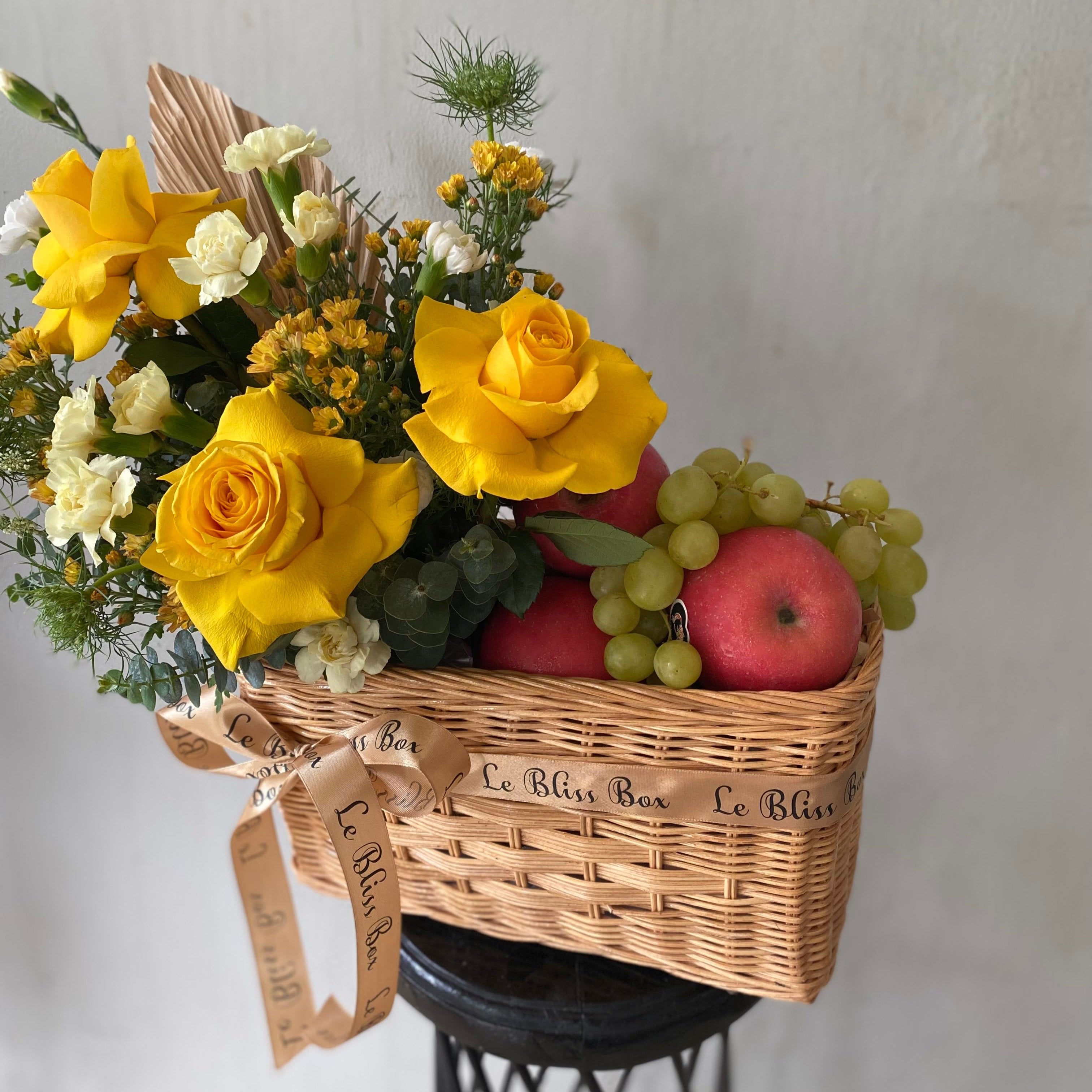 Keranjang anyaman cantik berisi buah-buahan segar dan bunga mawar kuning yang memikat, dipegang oleh seorang wanita dengan kemeja merah muda. Tersedia untuk pengiriman di Jakarta, Bintaro, Bogor, Bekasi, dan Depok.