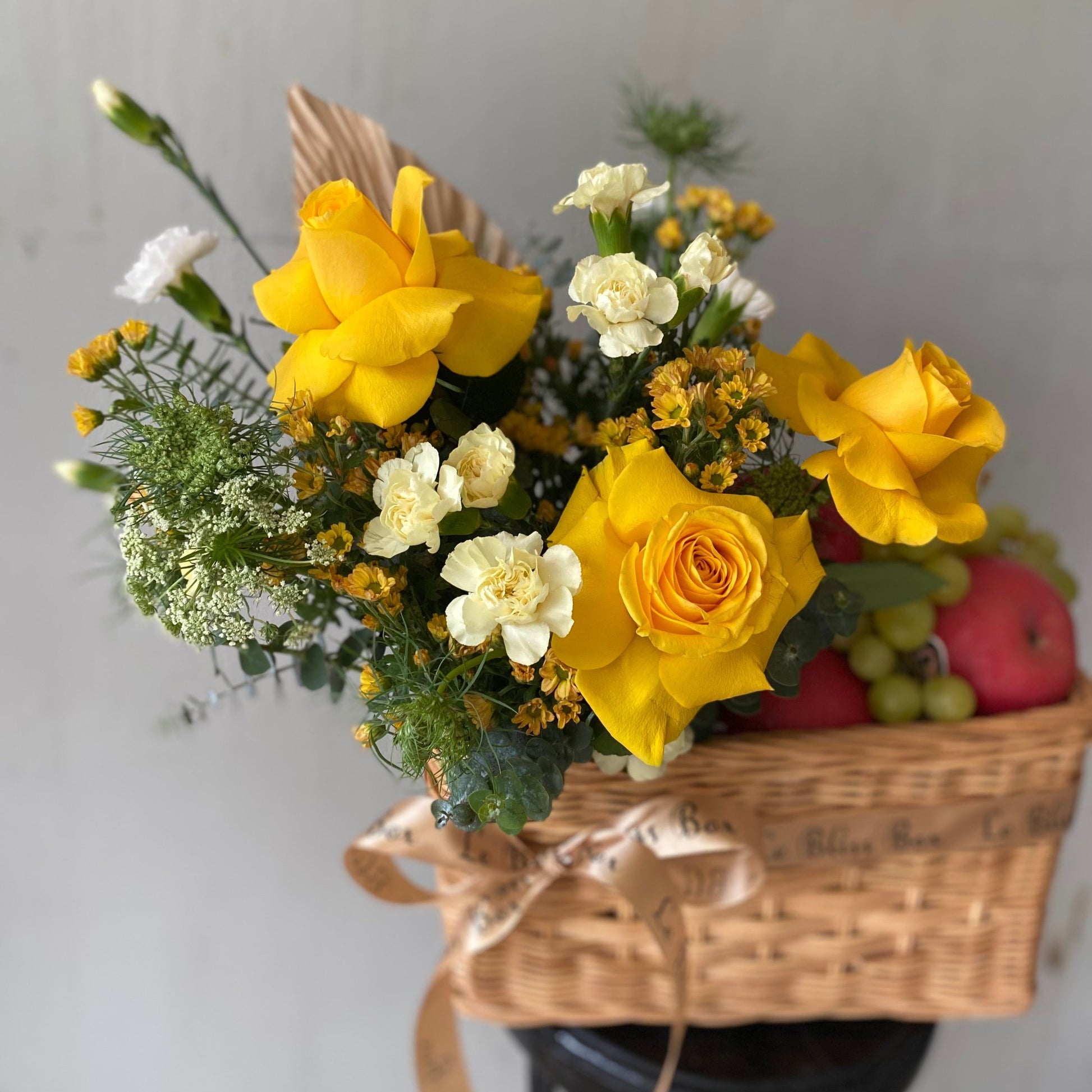 Keranjang anyaman cantik berisi buah-buahan segar dan bunga mawar kuning yang memikat, dipegang oleh seorang wanita dengan kemeja merah muda. Tersedia untuk pengiriman di Jakarta, Bintaro, Bogor, Bekasi, dan Depok.