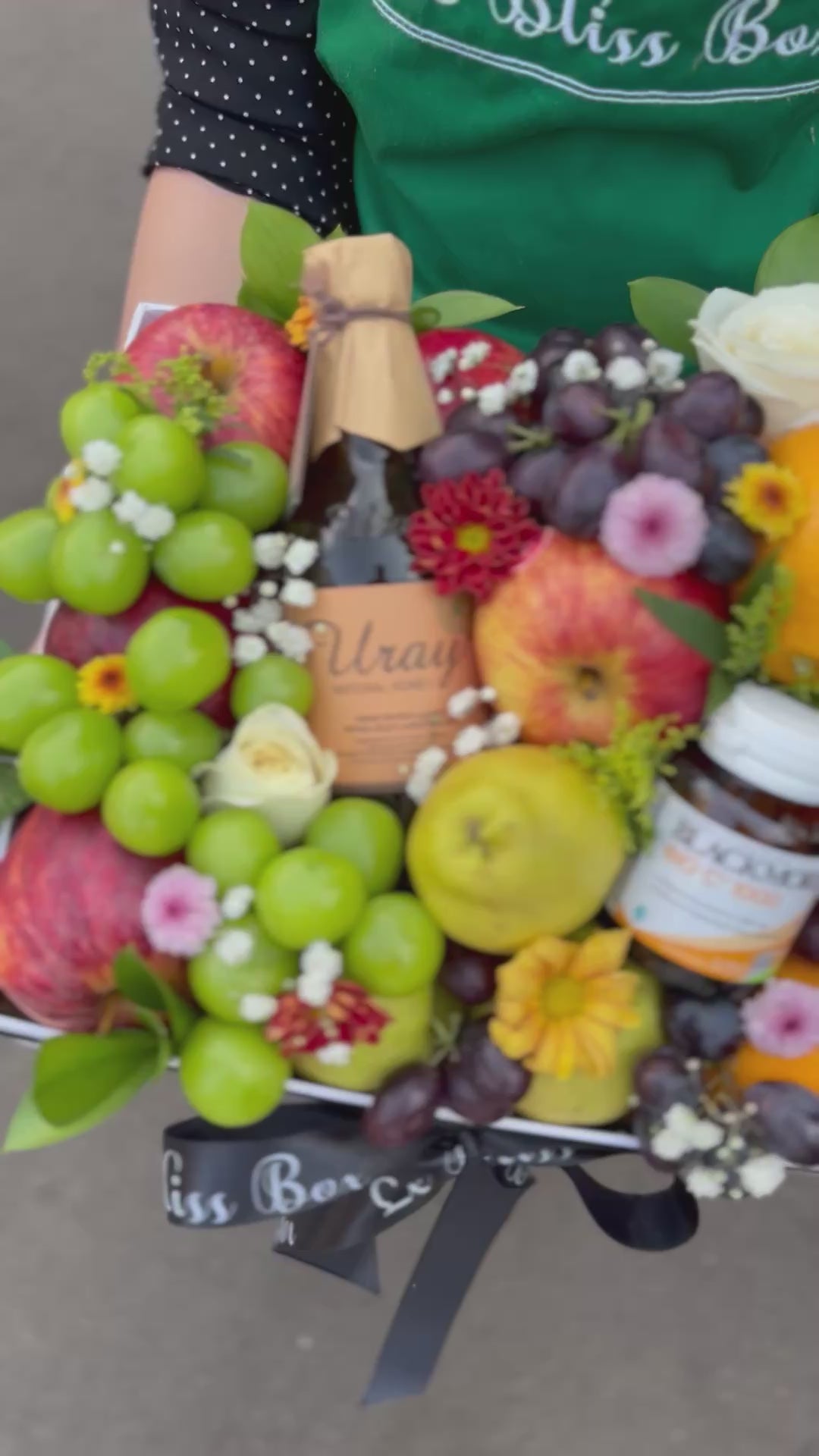 Fruit and flower arrangement with a person wearing a 'Le Bliss Box' apron. Person holding a box of fruits, flowers, and a bottle of wine with 'Le Bliss Box' branding. Parcel buah surabaya, parcel buah jakarta, parcel buah blackmores uray bintaro