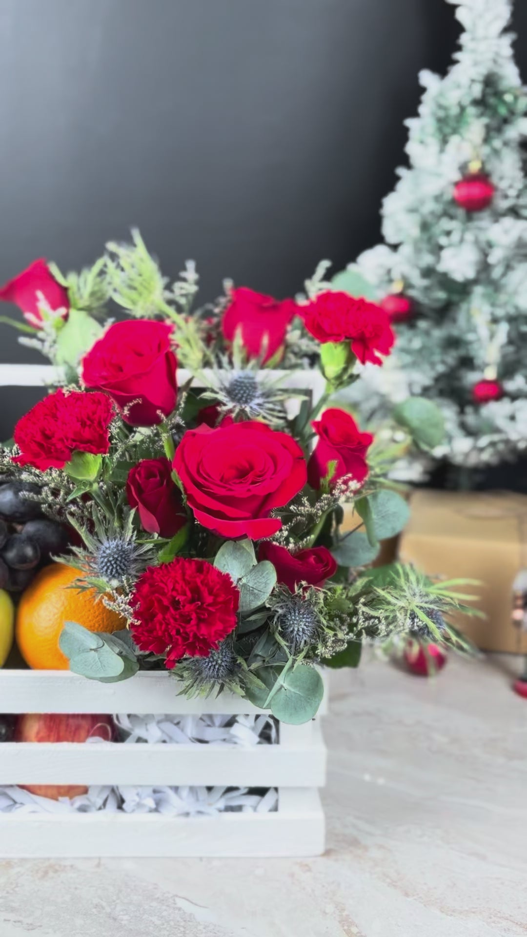Decorative fruit and flower arrangement in a white crate with Christmas decorations in the background. Blooming Red Crate Fruit Parcel | Best Christmas Hamper in Jakarta & Surabaya – Le Bliss Box